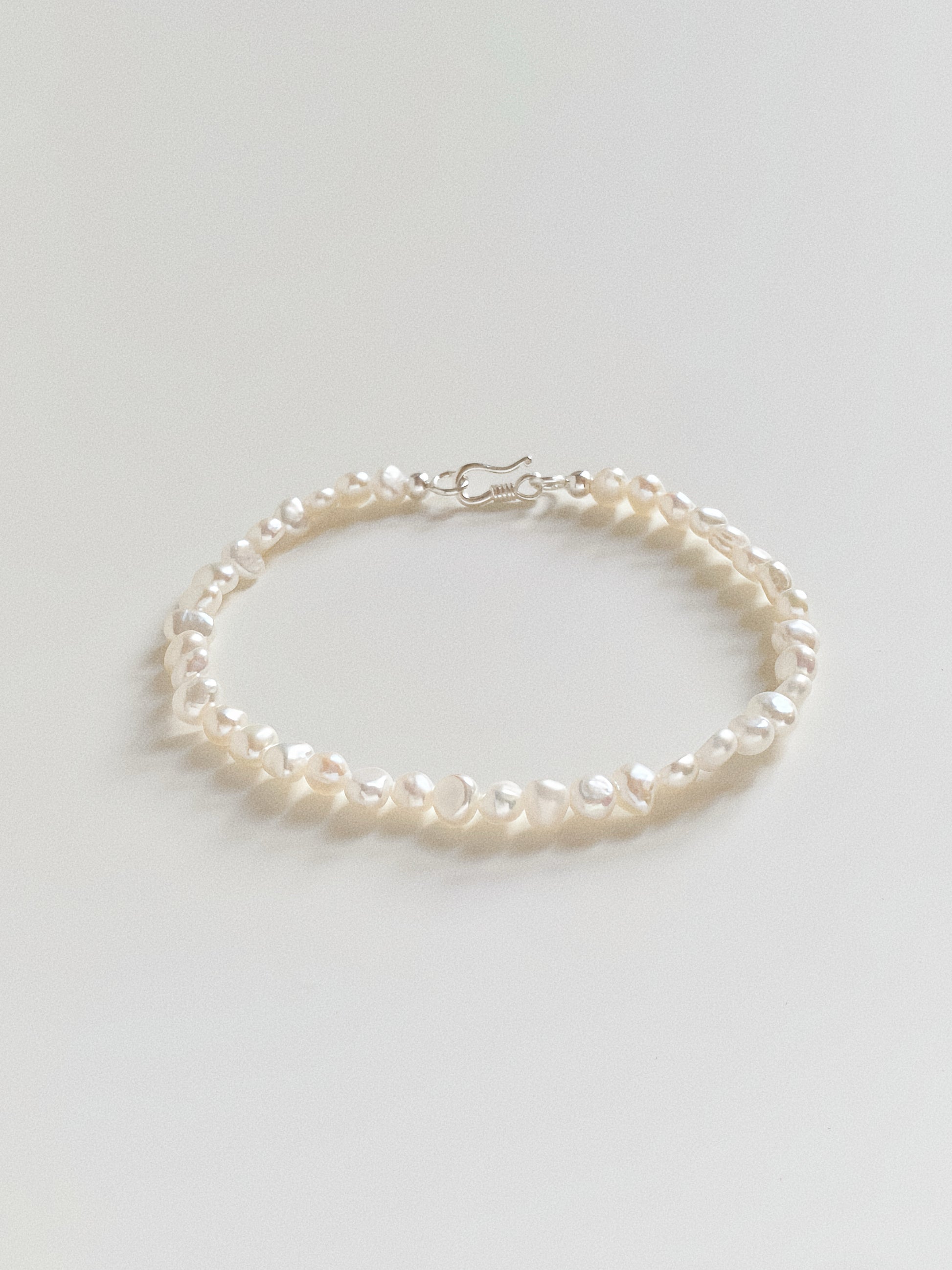 Flat lay of a dainty freshwater pearl bracelet featuring 4-5mm baroque pearls and a silver S-hook clasp.