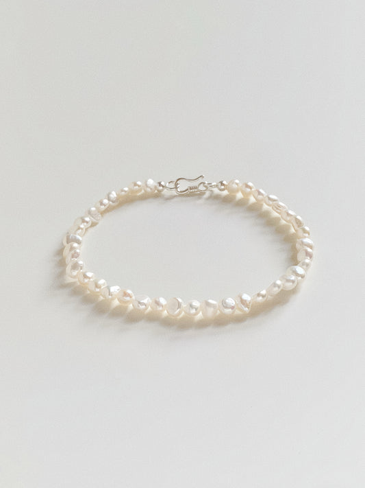 Flat lay of a dainty freshwater pearl bracelet featuring 4-5mm baroque pearls and a silver S-hook clasp.