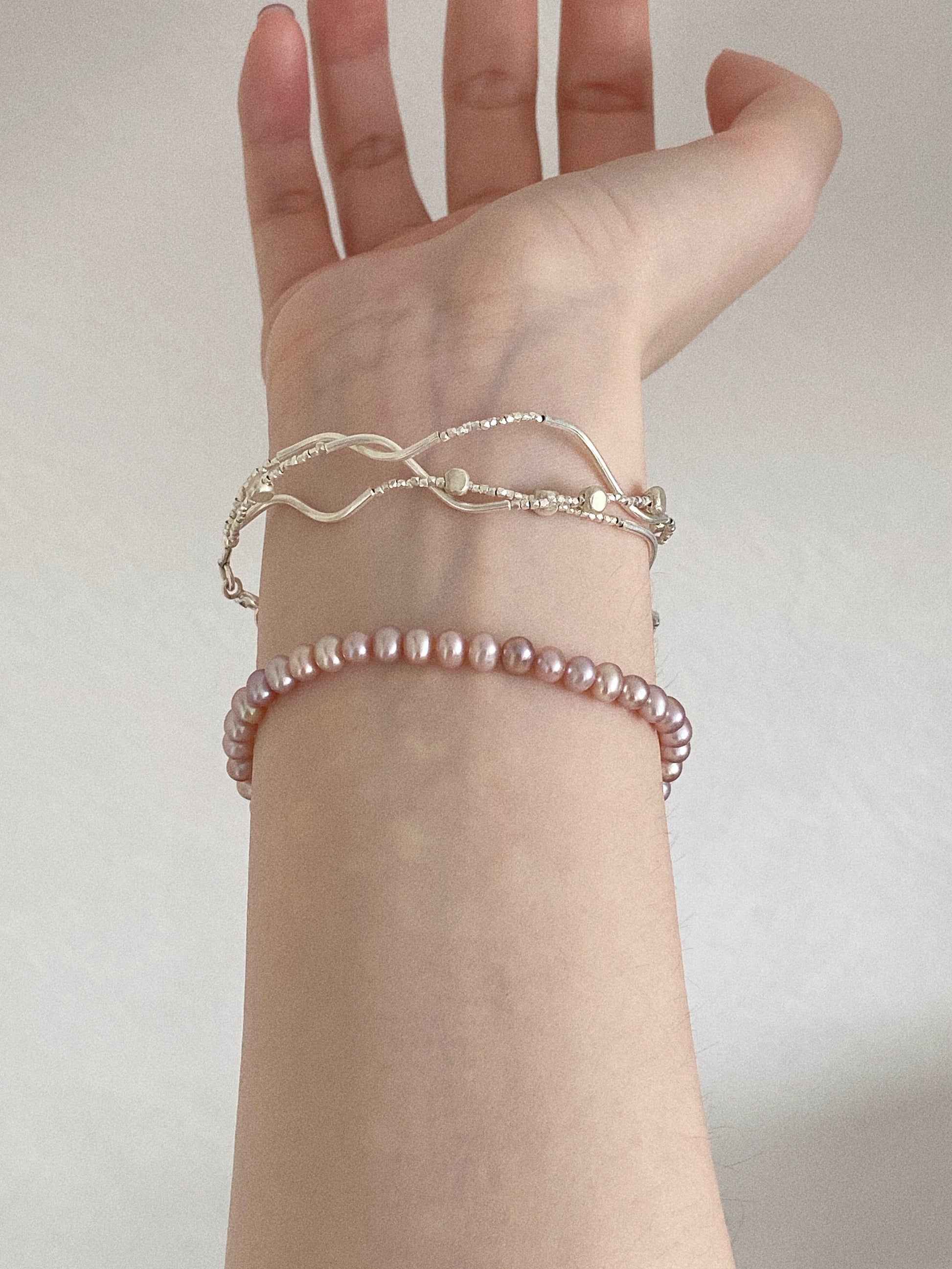 Natural pink lavender pearl bracelet on a slim wrist layered with fine silver bracelets, showing the soft mauve pearl tones