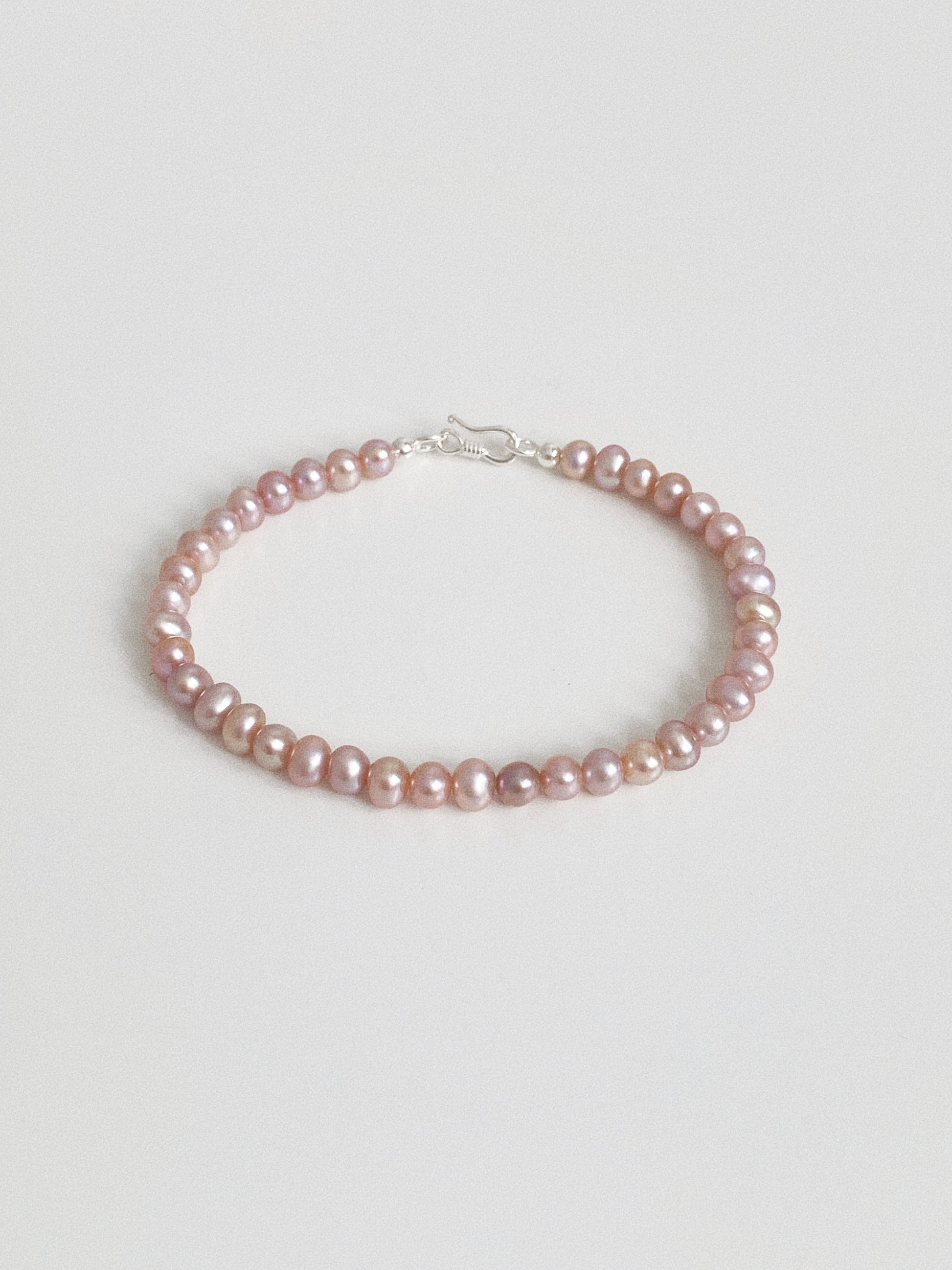 Flat lay of a natural pink and lilac freshwater pearl bracelet showing the soft iridescent lustre of small oval pearls