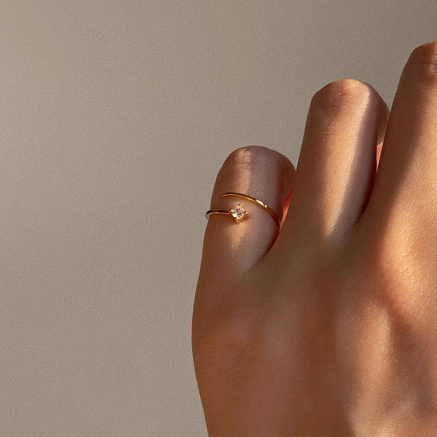 Adjustable gold wrap pinky ring with single sparkling stone on finger in warm natural sunlight