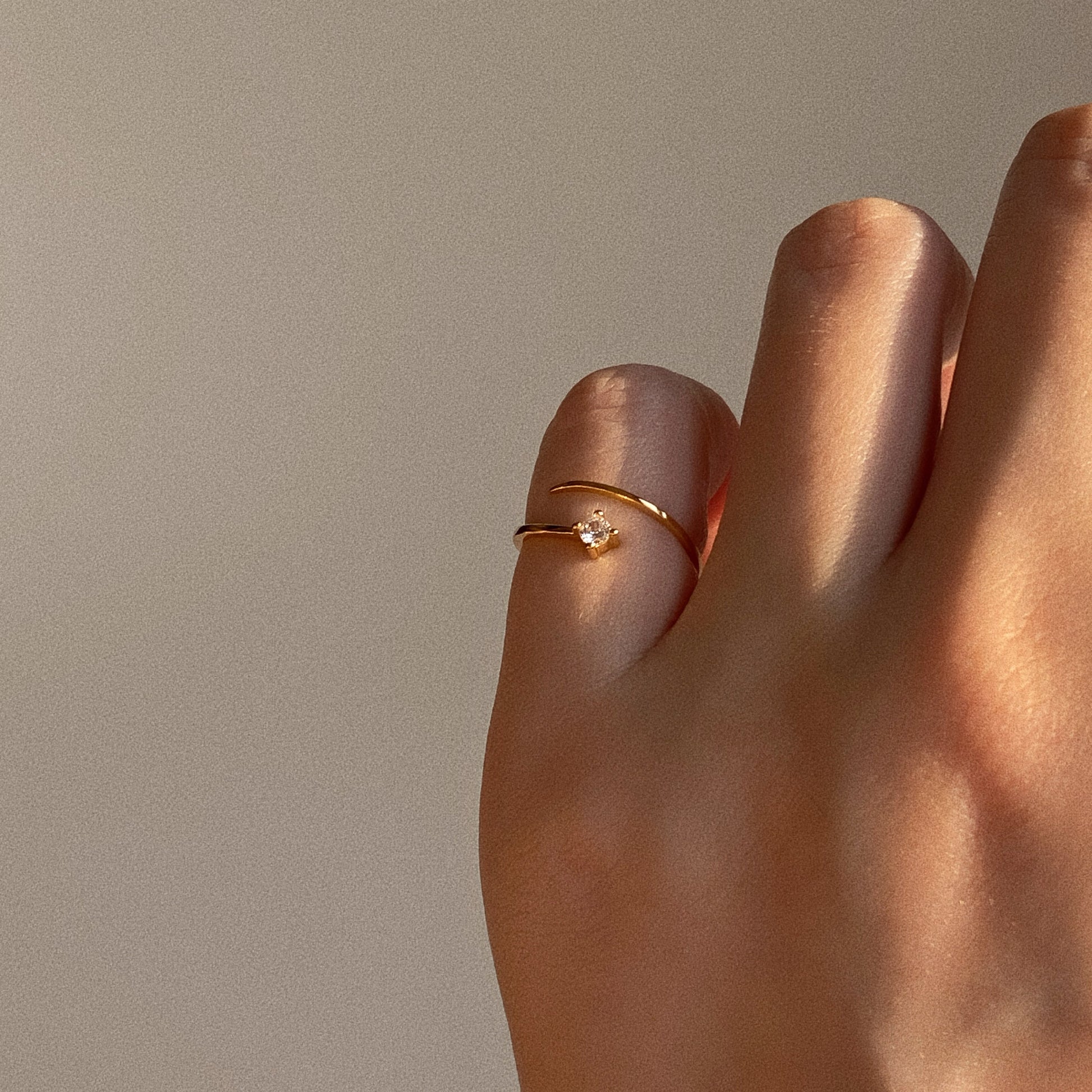 Adjustable gold wrap pinky ring with single sparkling stone on finger in warm natural sunlight