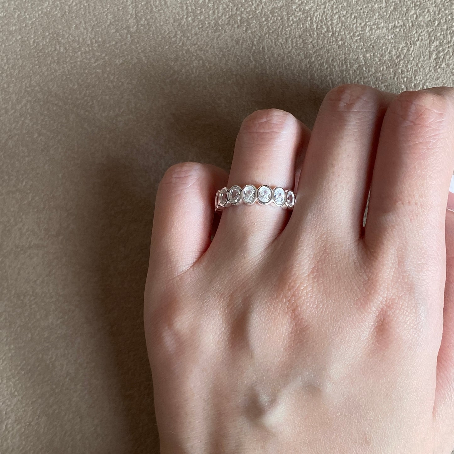 Ring on hand shot highlighting the oval bezel cubic zirconia sparkle, dainty sterling silver eternity wedding band for women.