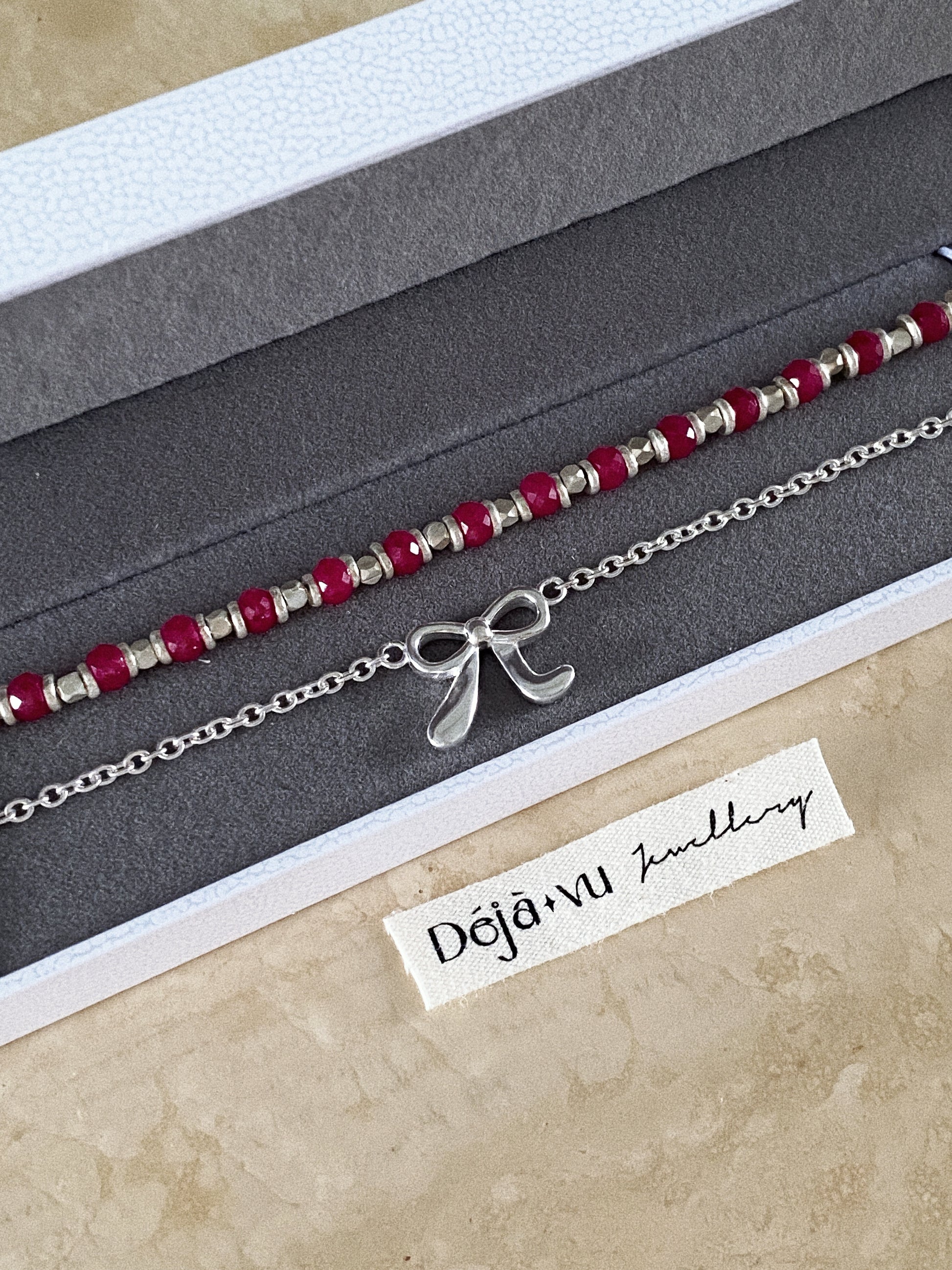 Red corundum bead bracelet in a Deja Vu Jewellery gift box, layered with a slim silver bow bracelet.