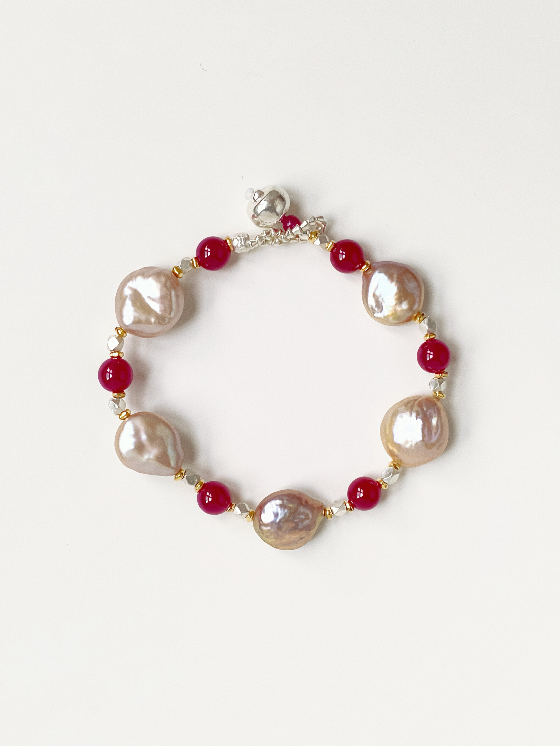 Handmade Roseate bracelet with oversized natural pink-purple baroque pearls and red corundum gemstones on a white background.