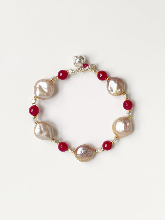 Handmade Roseate bracelet with oversized natural pink-purple baroque pearls and red corundum gemstones on a white background.
