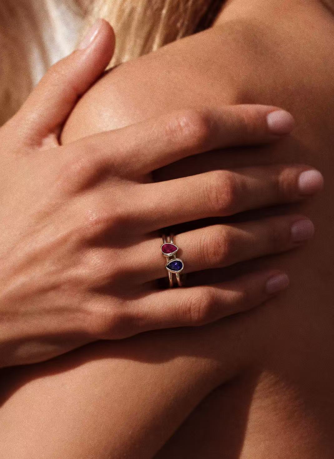 Ruby teardrop ring stacked with a blue gemstone ring on a finger; styling image