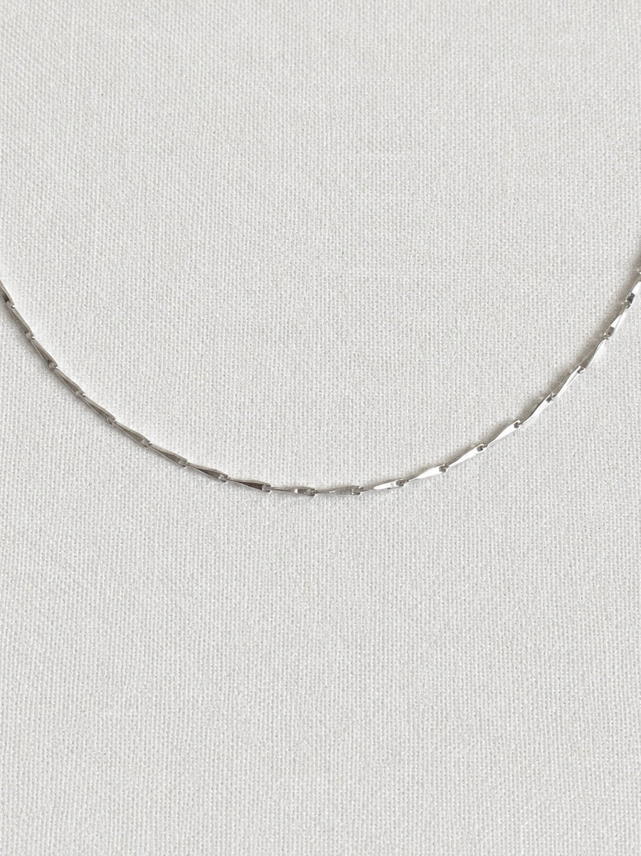 Fine faceted 925 sterling silver bar chain necklace shown close up on a white linen background, shimmering delicate everyday chain