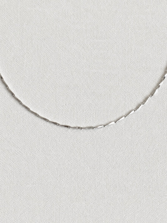 Fine faceted 925 sterling silver bar chain necklace shown close up on a white linen background, shimmering delicate everyday chain