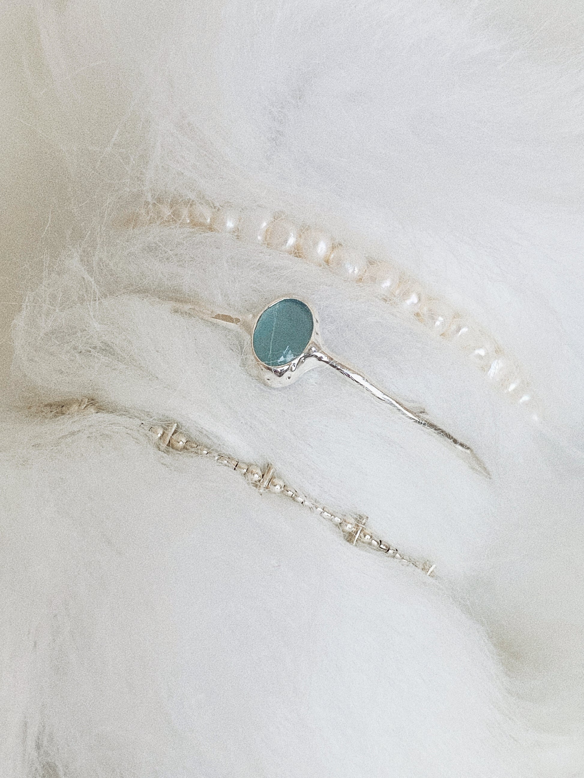 Wrist stack styling with aquamarine cuff bangle layered between pearl and silver bead bracelets