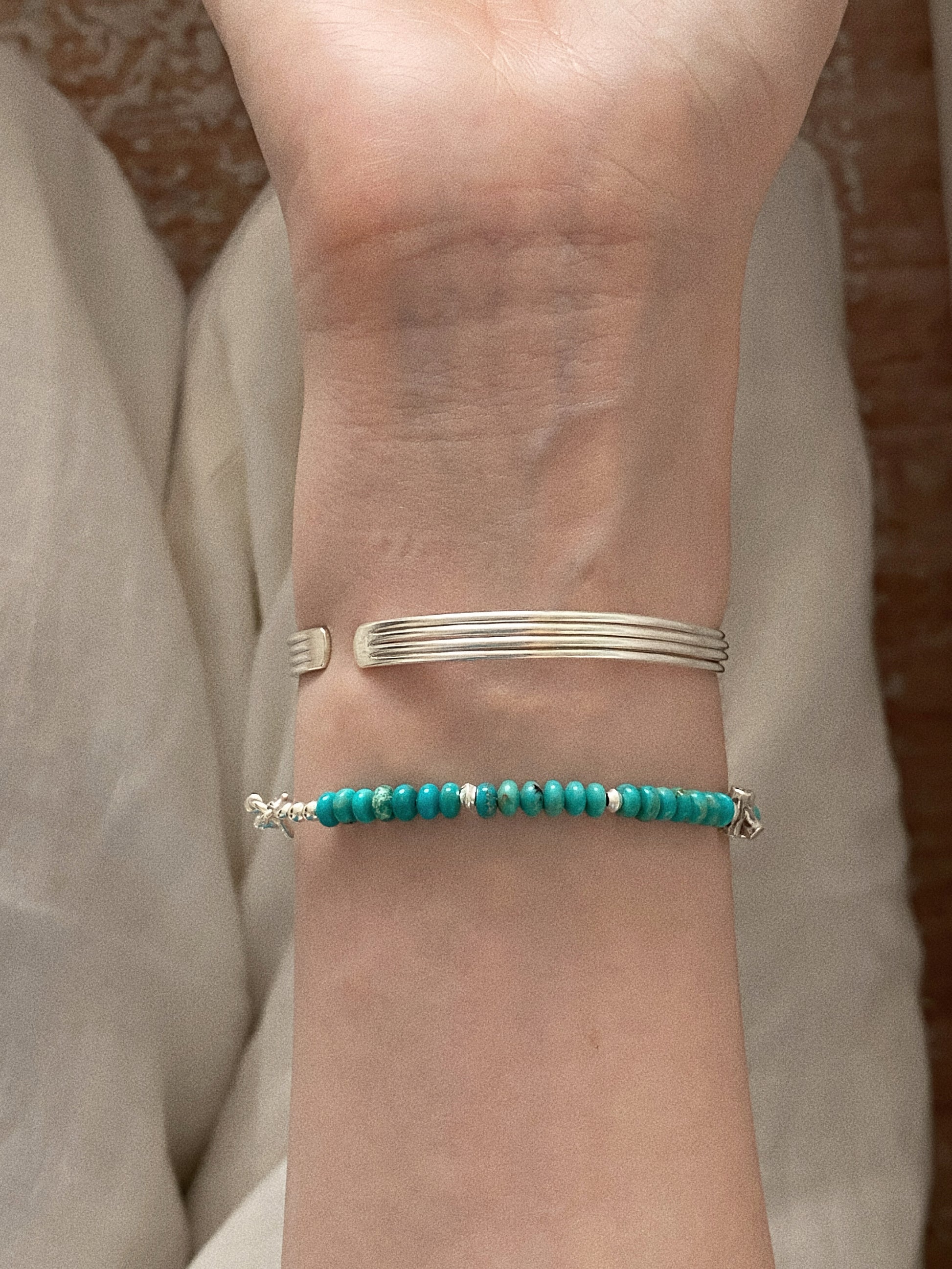 Front view of the turquoise beaded bracelet and ribbed silver cuff worn together on one wrist