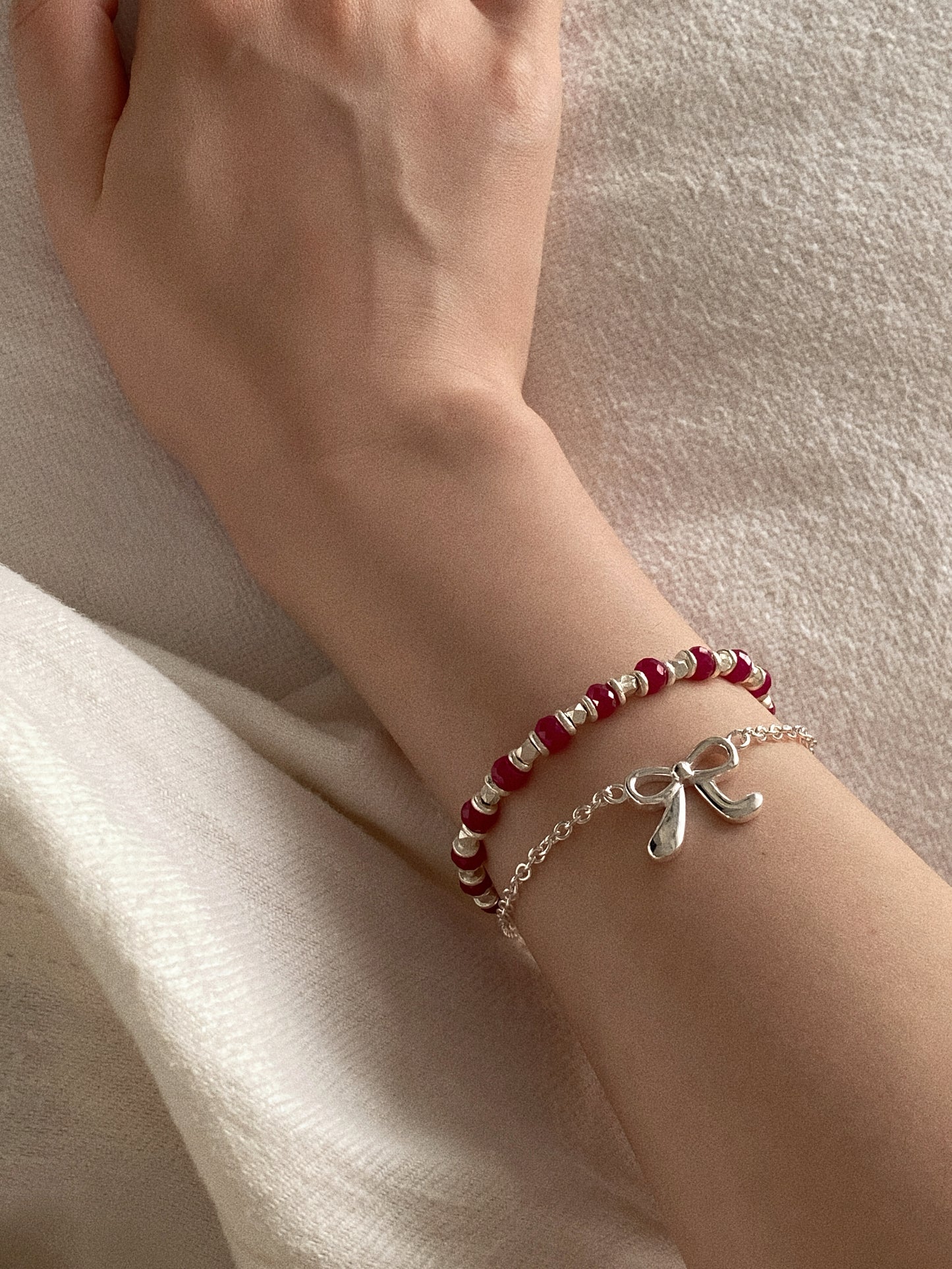 Ballet bow bracelet in 925 sterling silver worn on the wrist, layered with the Berry red corundum bead bracelet.