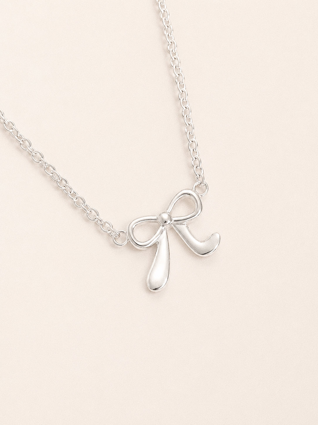 Close view of the silver bow bracelet, a polished sculpted bow with looped ends and flared tails on a belcher chain.