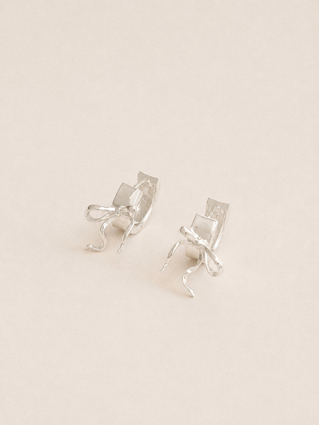 Back view of silver bow huggie earrings showing the wide hinged hoops and 925 sterling silver posts.