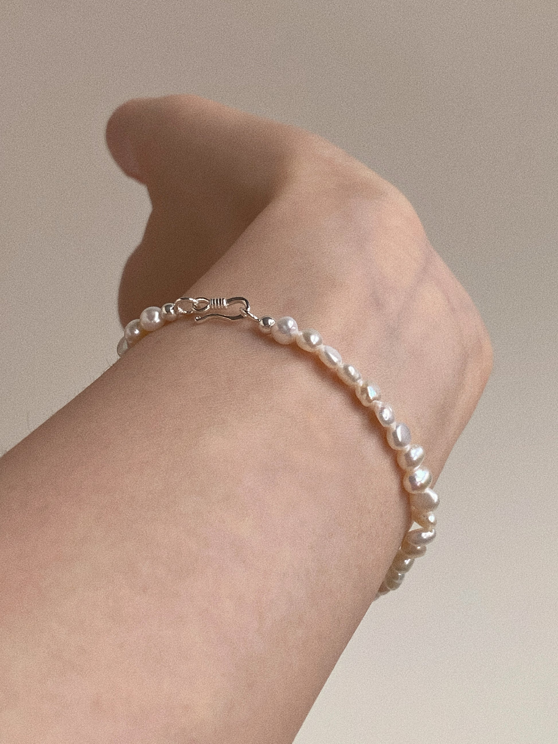 Side view of wrist wearing the pearl bracelet, highlighting the silver S-hook clasp detail against the skin.