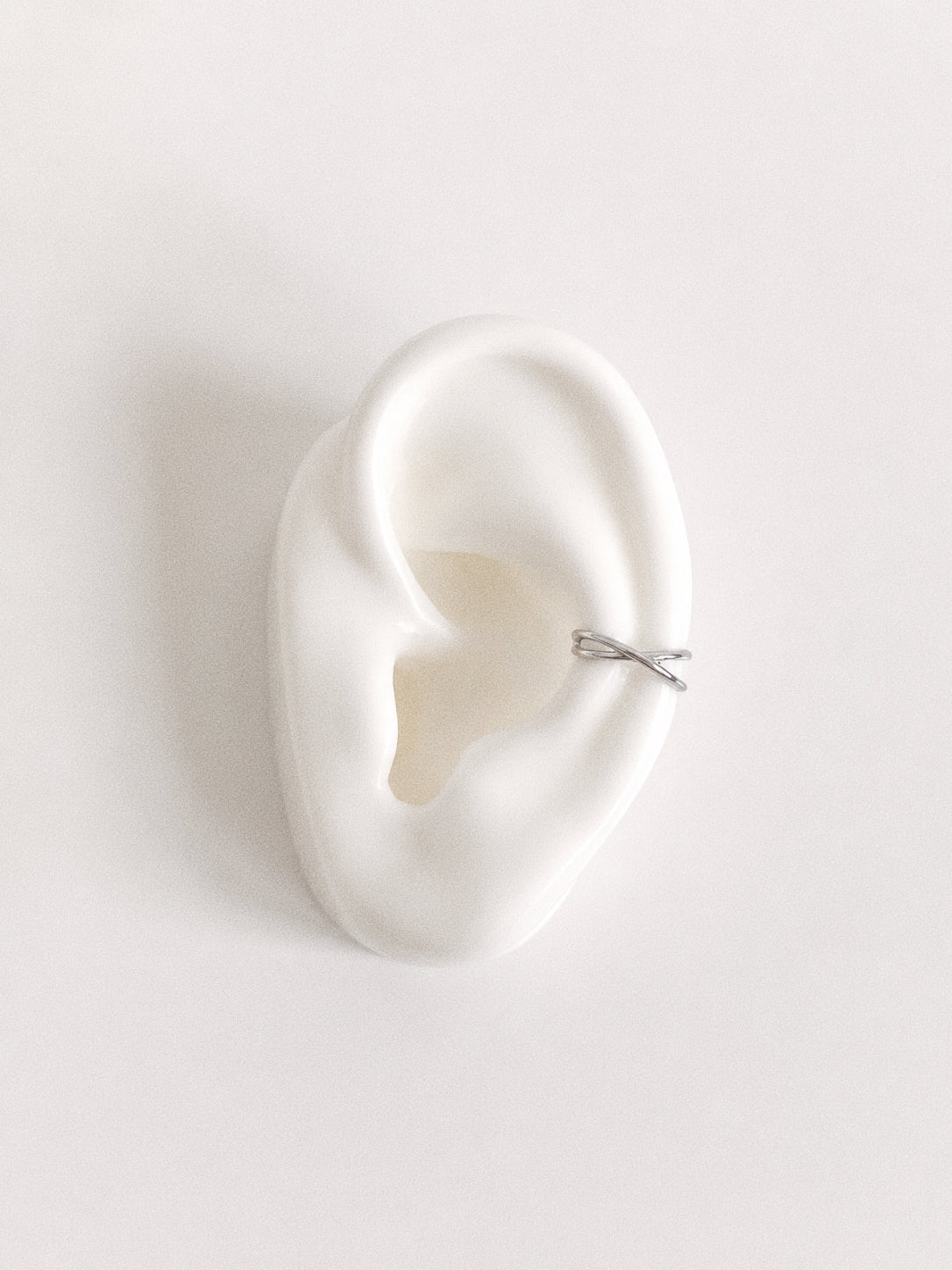 Sterling silver criss cross ear cuff sitting on the outer cartilage of a ceramic ear display, no piercing ear cuff