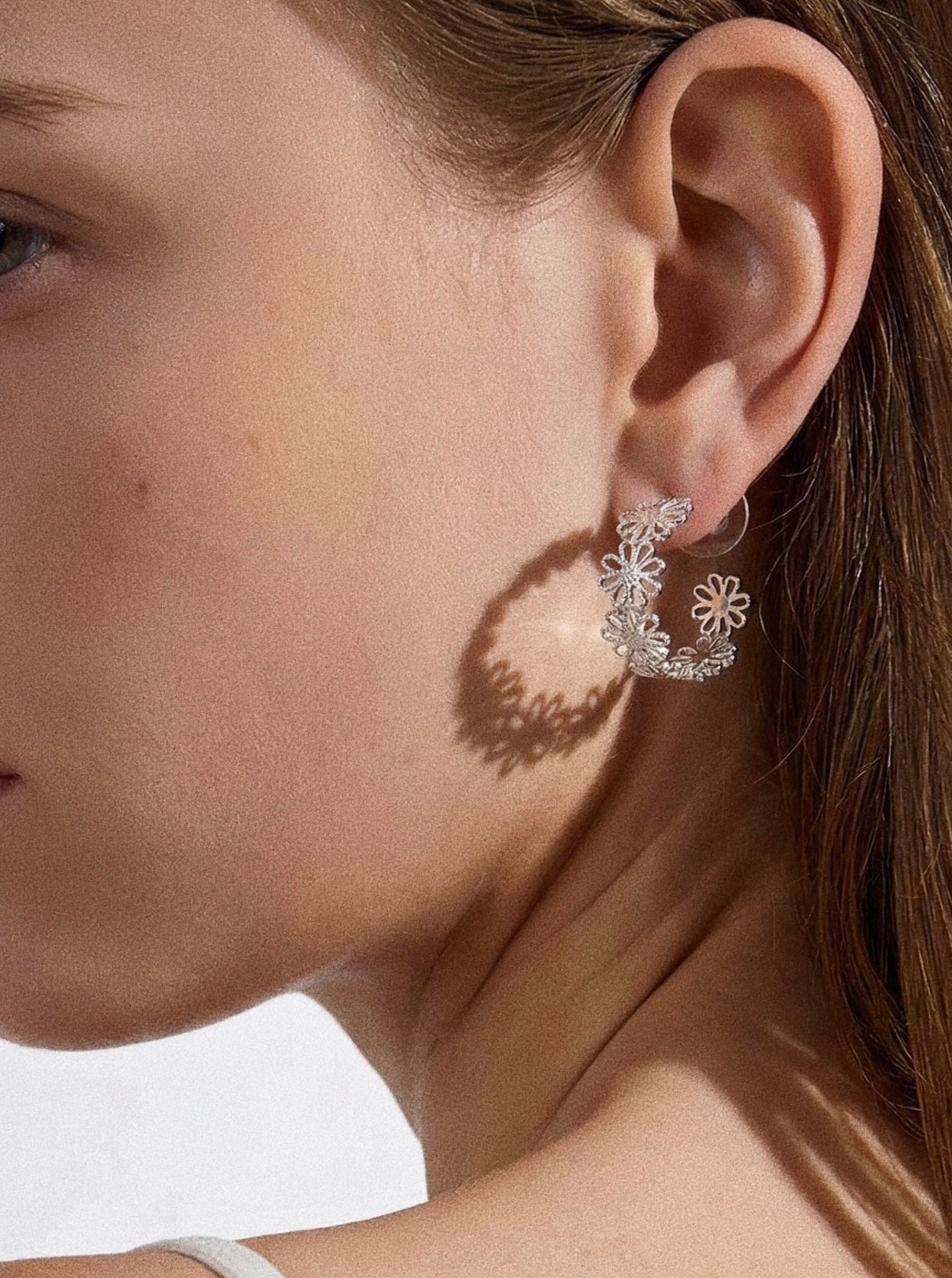 Silver daisy lace open hoop earring styled on model with hair back showing full floral hoop detail