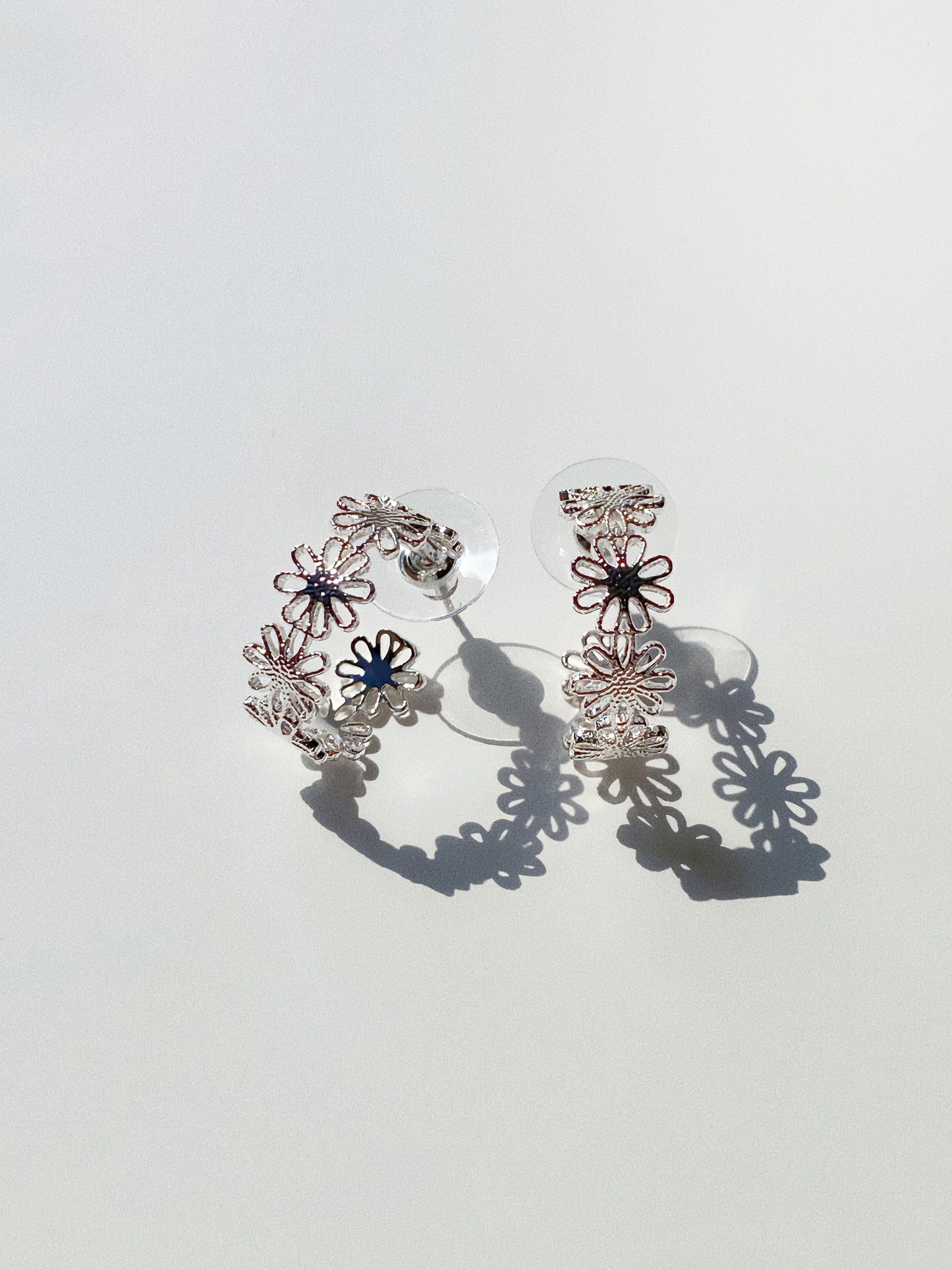 Silver daisy lace open hoop earrings showing cut-out floral pattern and delicate shadow