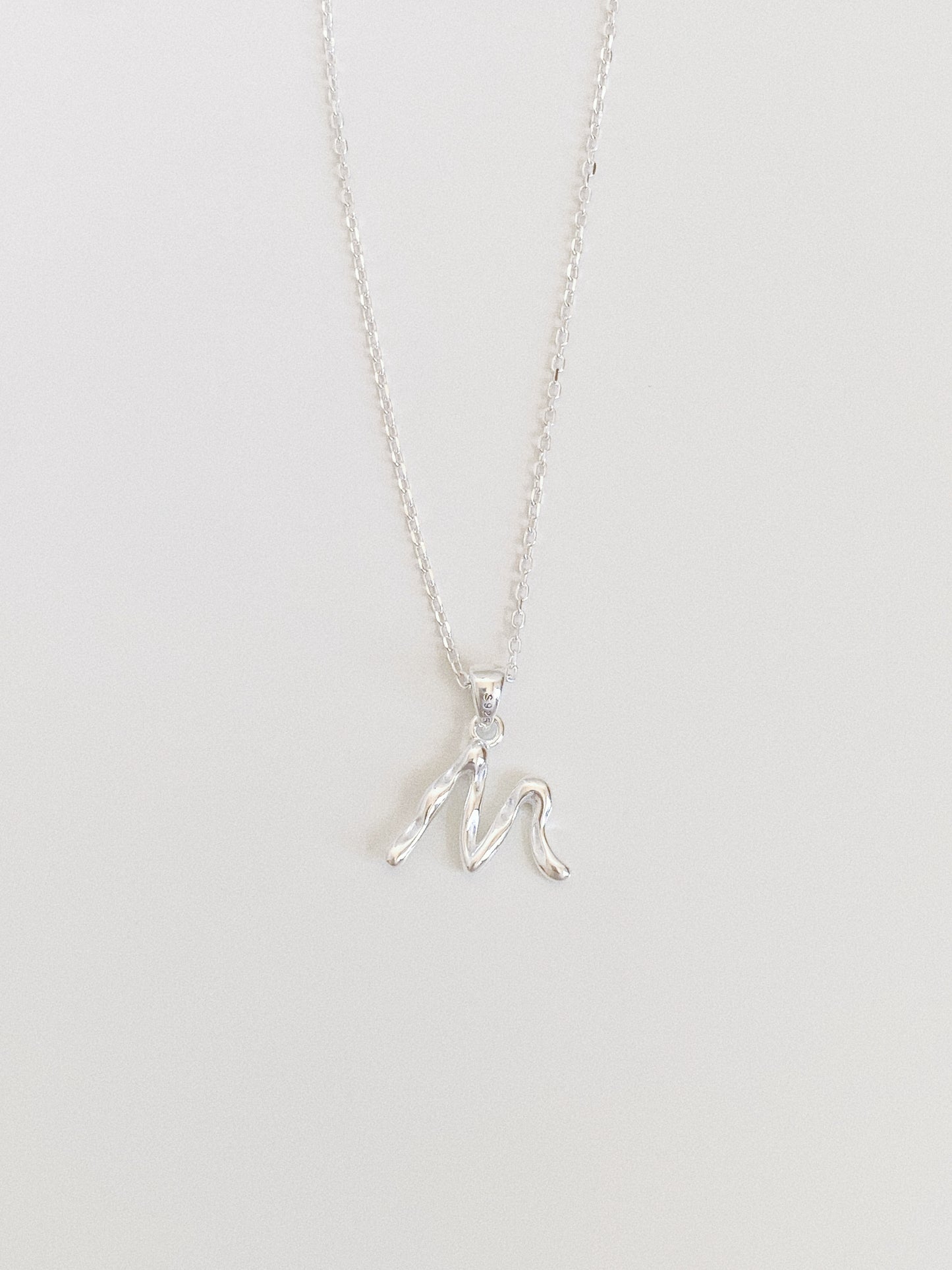 Dainty sterling silver initial necklace with a flowing script letter M pendant on a fine cable chain
