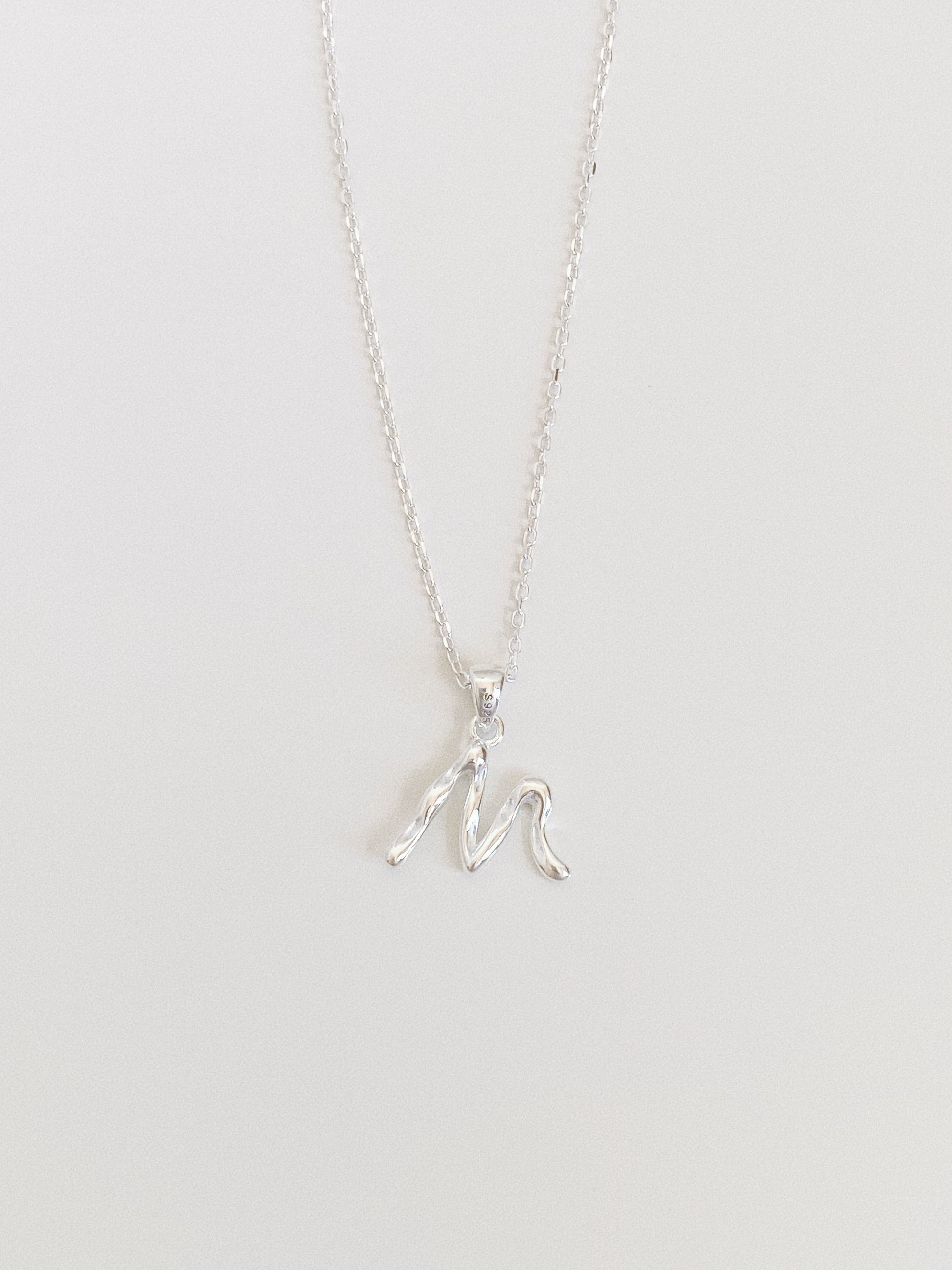 Dainty sterling silver initial necklace with a flowing script letter M pendant on a fine cable chain