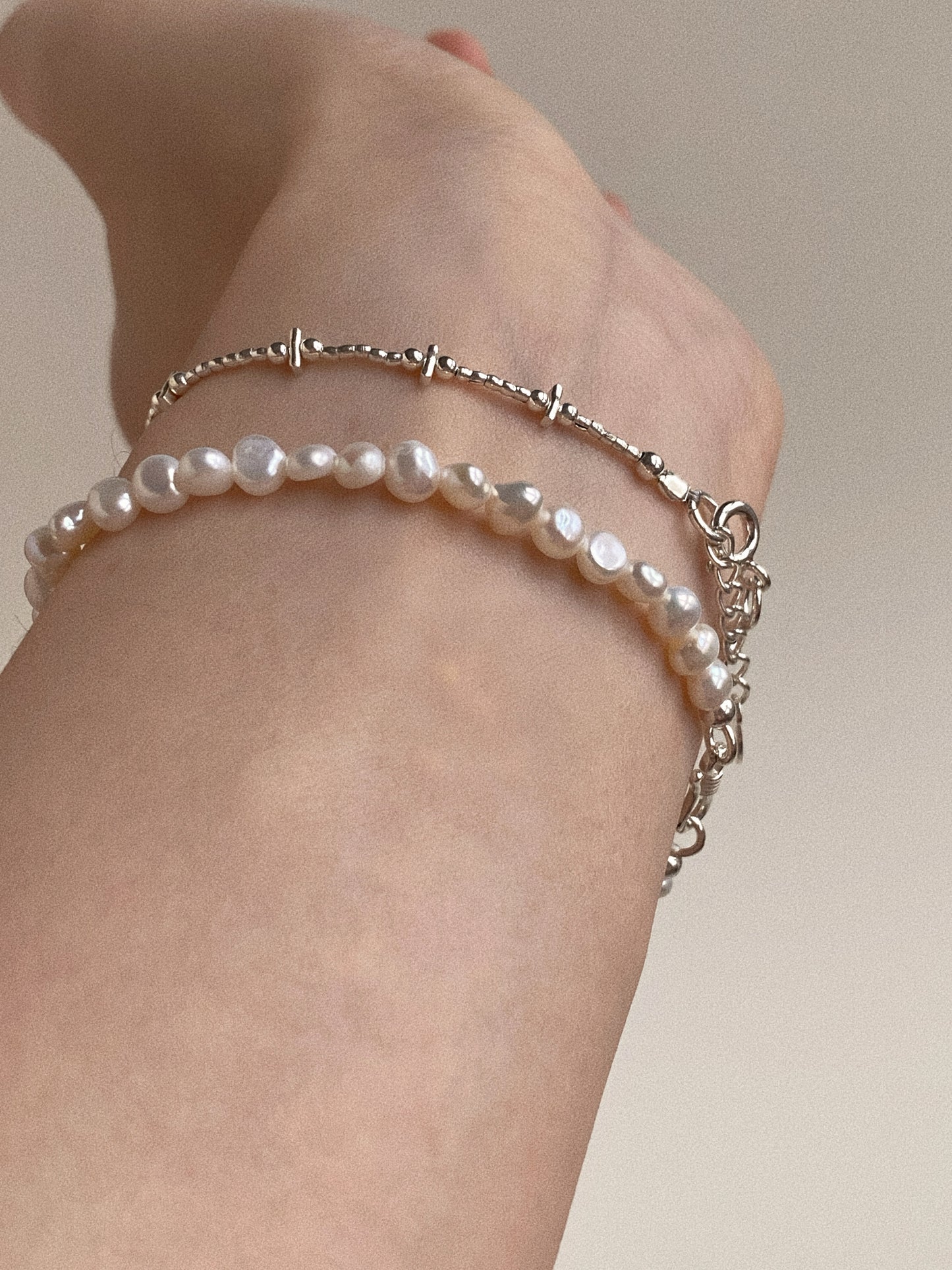 Side view of a woman's wrist wearing a stack of handmade silver and pearl bracelets, perfect for everyday styling.