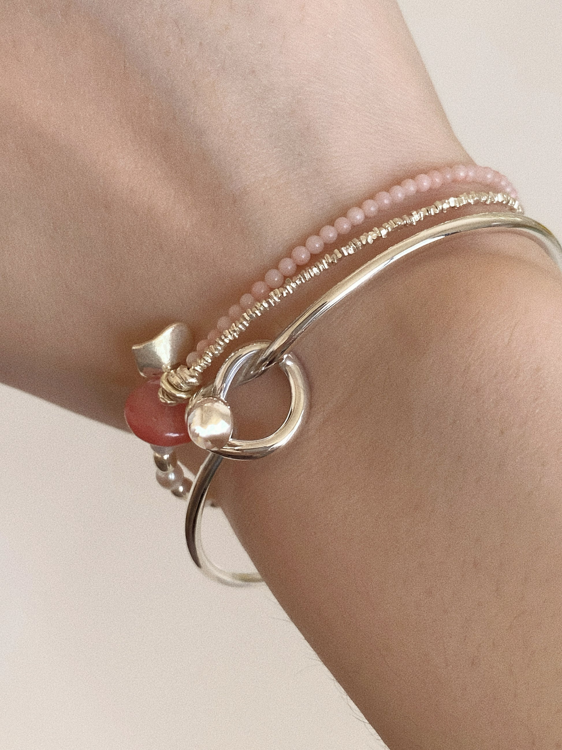 Sterling silver love knot bangle stacked with delicate pink beaded bracelets on the wrist, showing the knot detail