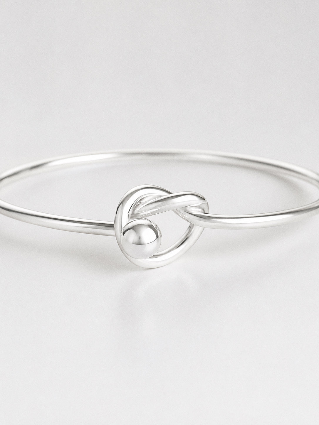 Close-up of the hand-shaped knot and polished silver ball on a 925 sterling silver love knot bangle