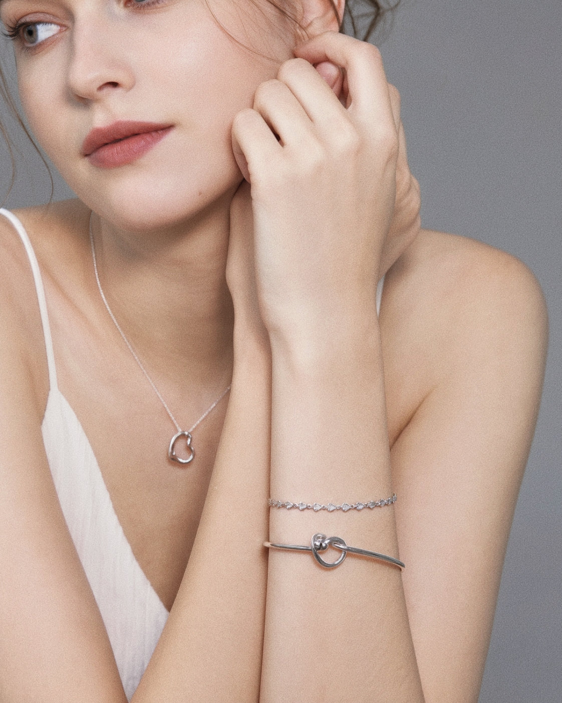 Model wearing the sterling silver love knot bangle stacked with a heart bracelet and a silver heart pendant necklace