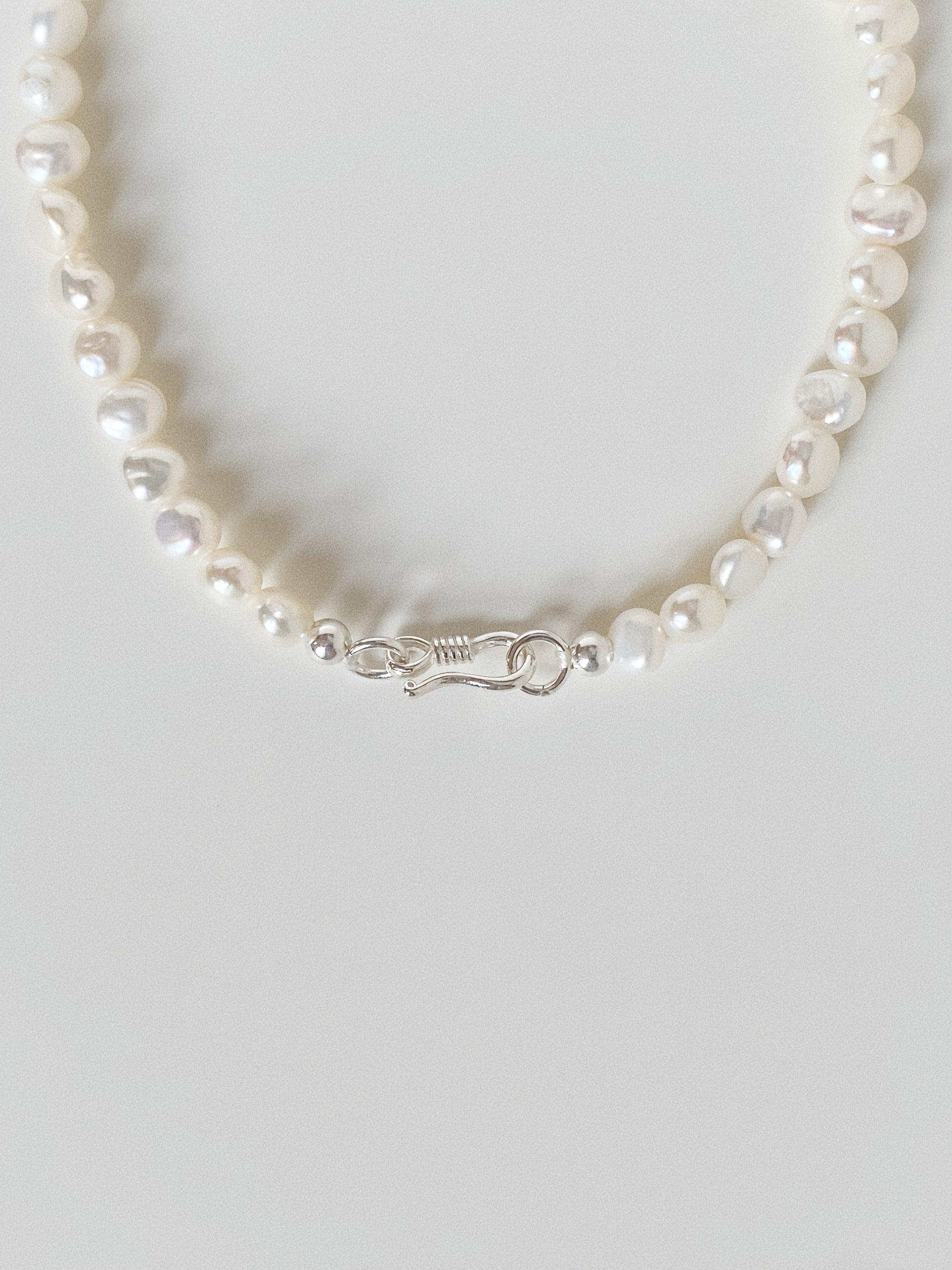 Close up detail of the handcrafted 925 sterling silver S-hook clasp on a small pearl bracelet.