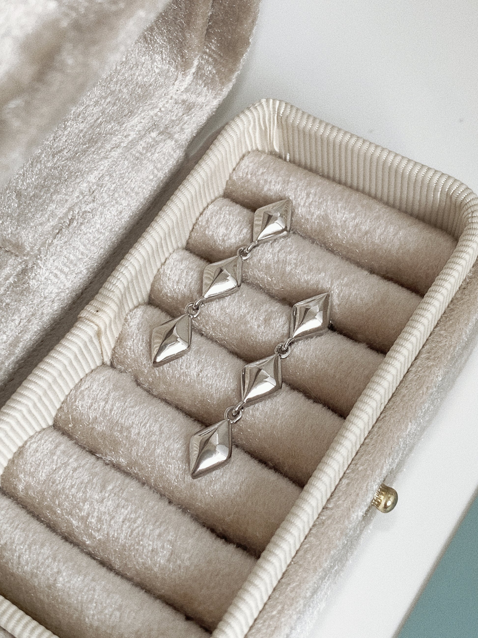 Silver Vega star drop earrings resting in a cream velvet jewellery case.