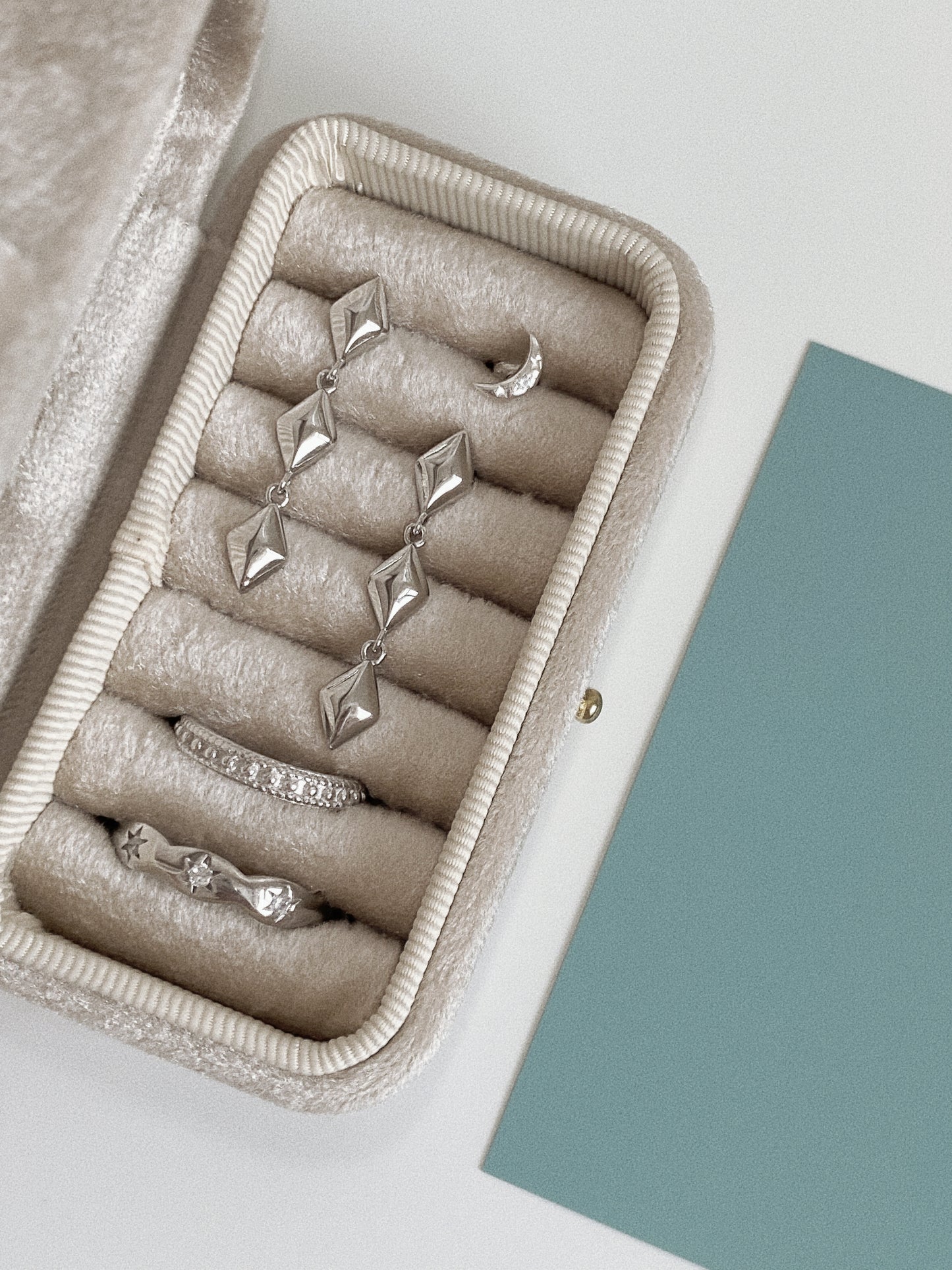 Silver star drop earrings in a velvet jewellery case, shown alongside a crescent stud and two silver rings.