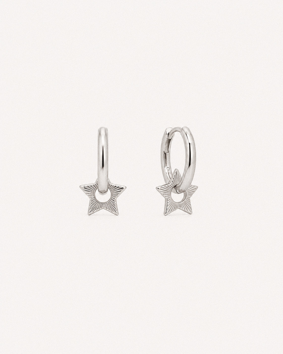 Silver star huggie hoop earrings with engraved sunburst star charms hanging from smooth 925 hoops.