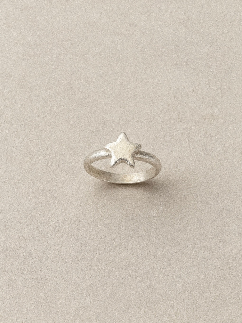 Handmade star ring standing upright in brushed 925 sterling silver on a soft neutral backdrop.
