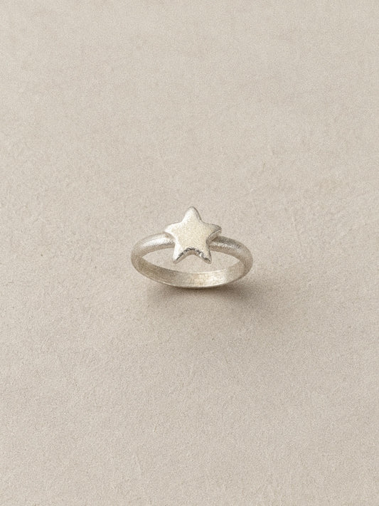 Handmade star ring standing upright in brushed 925 sterling silver on a soft neutral backdrop.