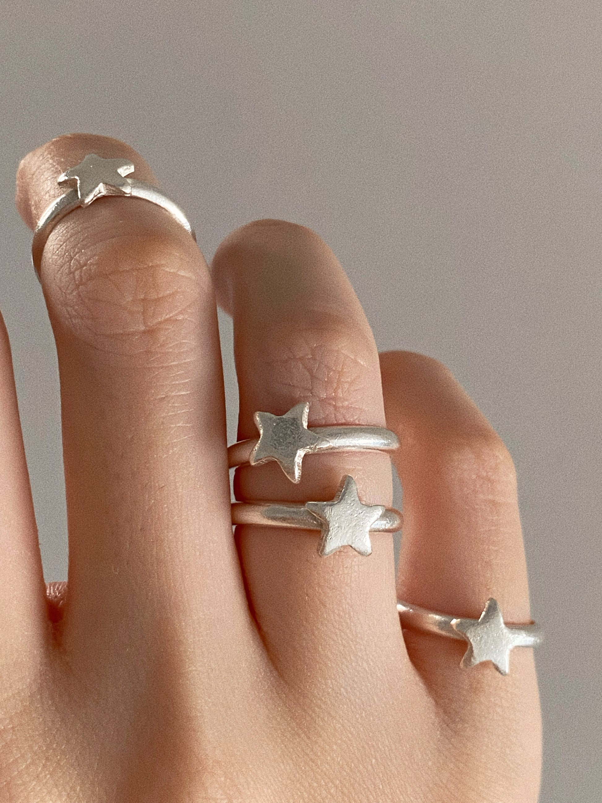 Four handmade sterling silver star rings stacked across one hand, each hand finished star slightly different.