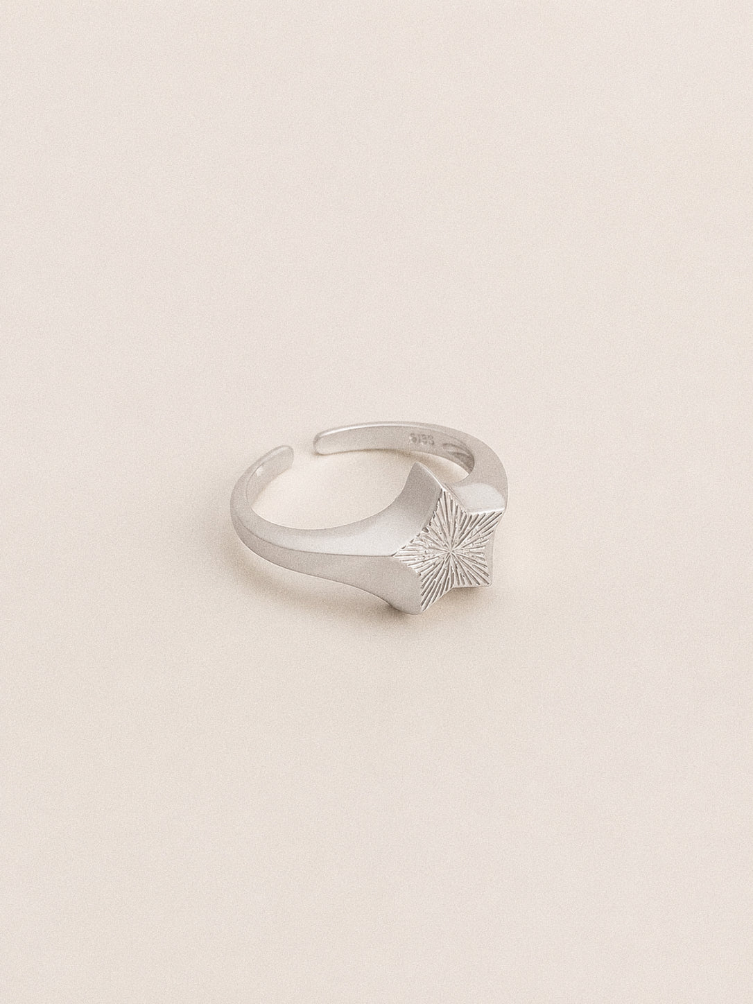 Silver star signet ring at an angle, fine engraved rays across the star face and a 925 stamp inside the band.