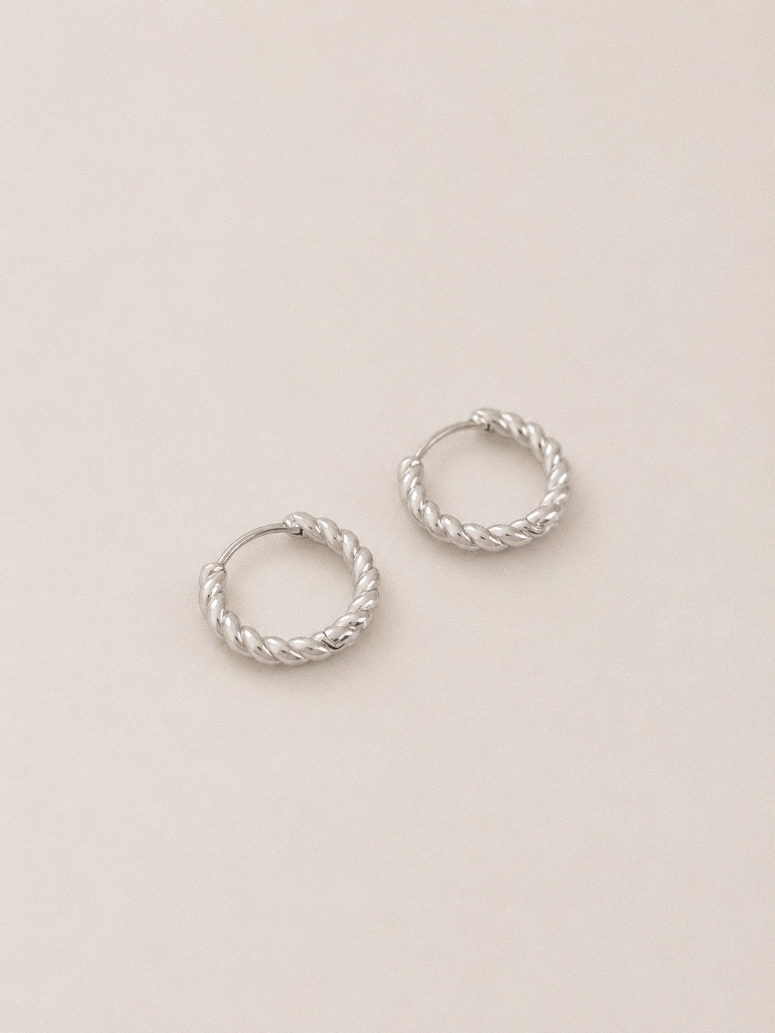 Pair of sterling silver twisted rope huggie hoops with hinged closure on a soft cream background