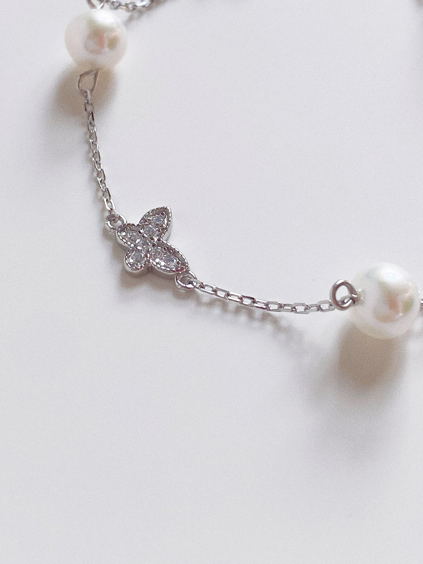 Close up detail of the sparkling pavé crystal butterfly charm and high-luster 6mm pearl on a silver chain.