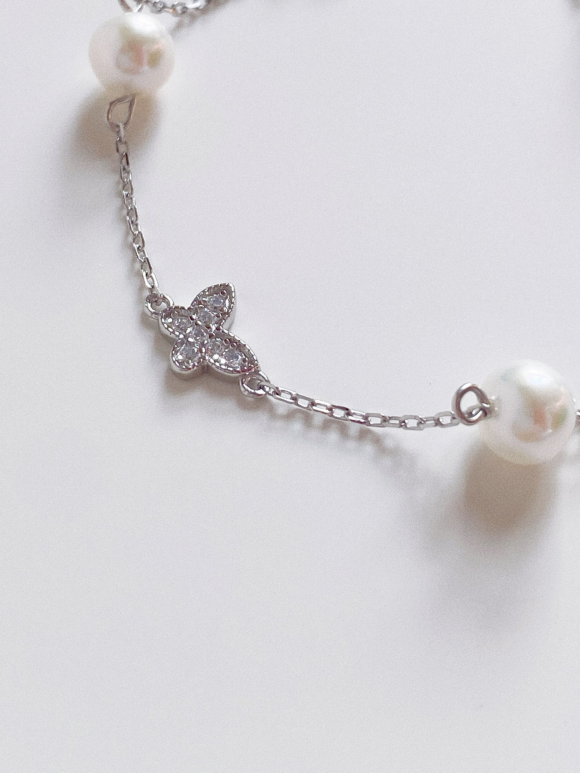 Close up detail of the sparkling pavé crystal butterfly charm and high-luster 6mm pearl on a silver chain.