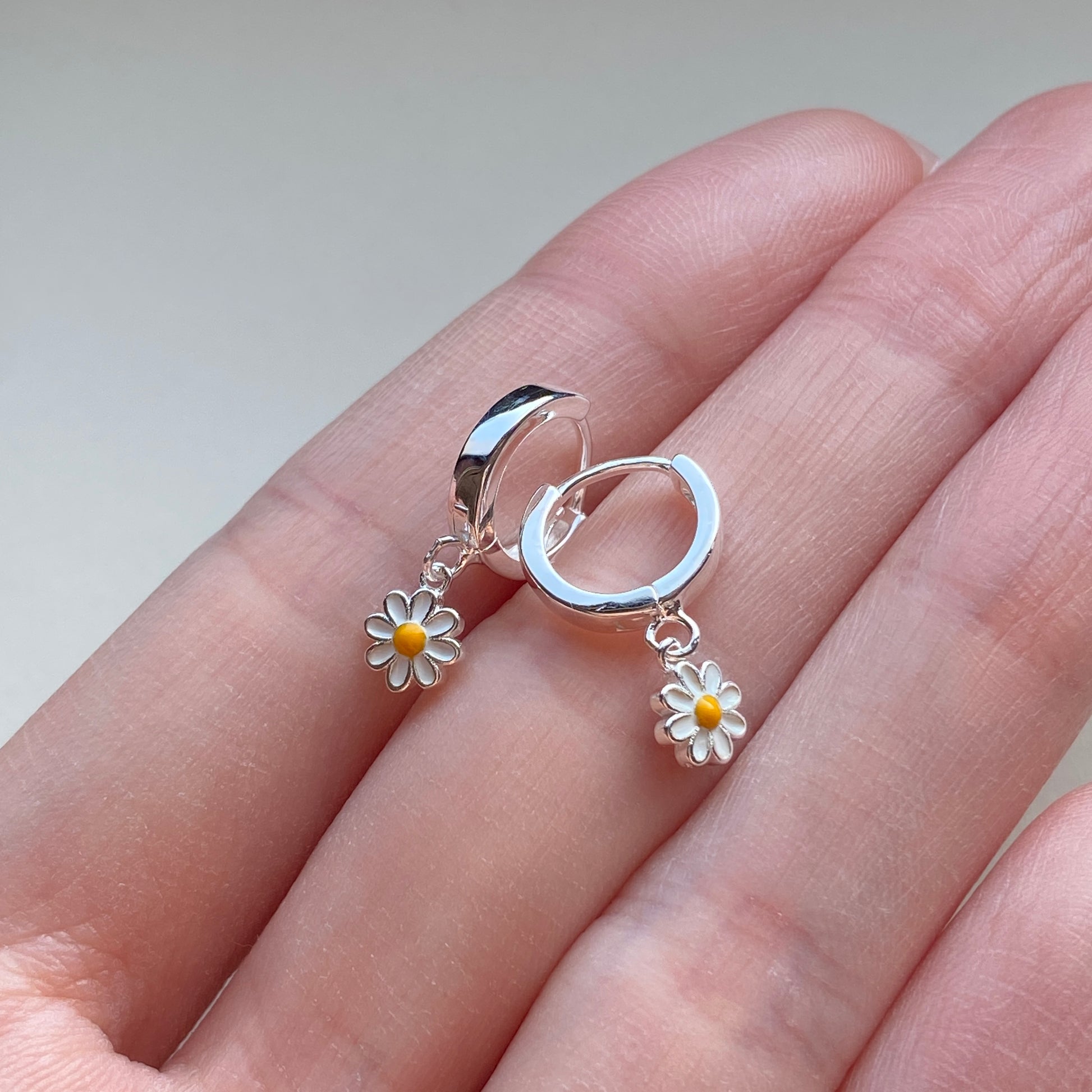 Tiny daisy charm dangling from 10 mm sterling-silver huggie hoop on hand