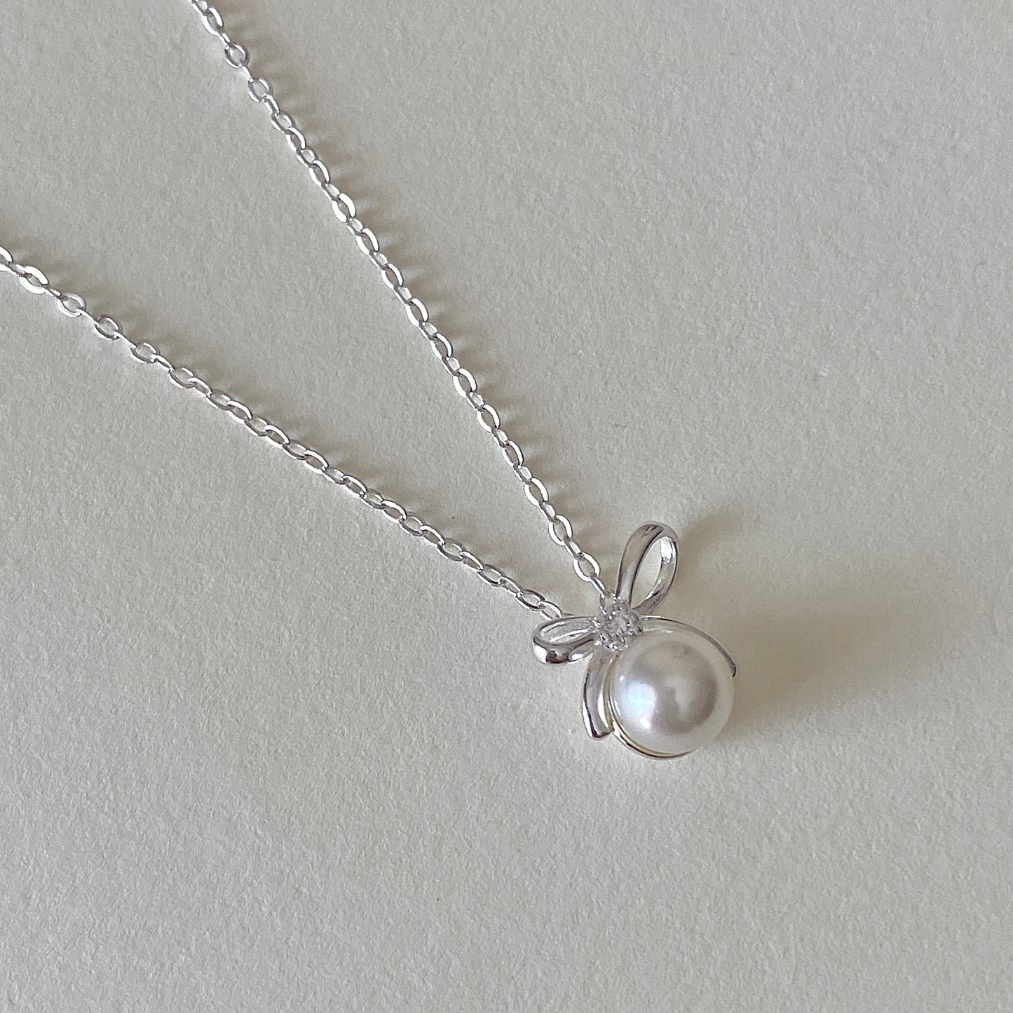 Silver bow pearl pendant with tiny accent stone at knot, minimal pearl necklace