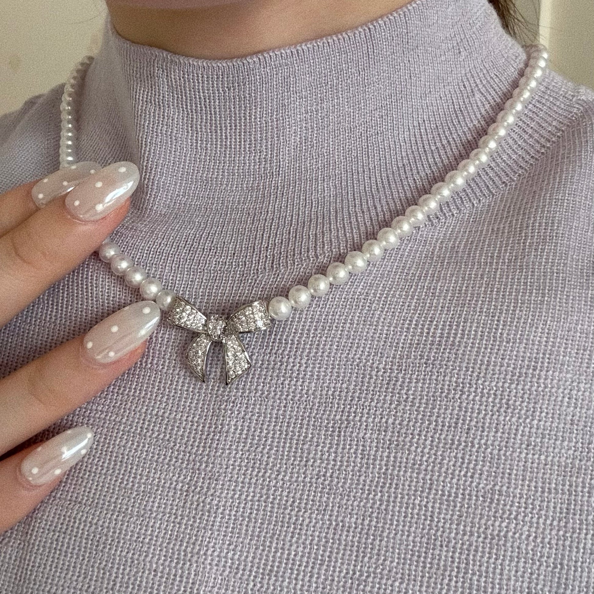 Close up of 5-6mm freshwater pearl necklace with a silver bow charm, styled with a cozy lavender sweater.