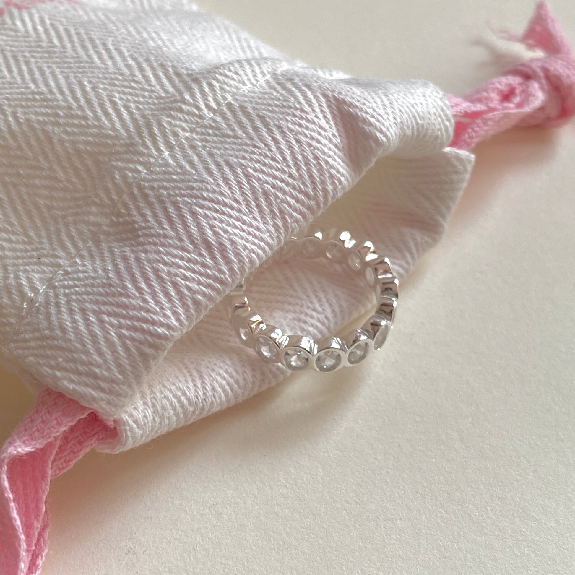 Oval bezel eternity ring peeking from a soft jewelry pouch, gift-ready sterling silver stacking ring for everyday wear.