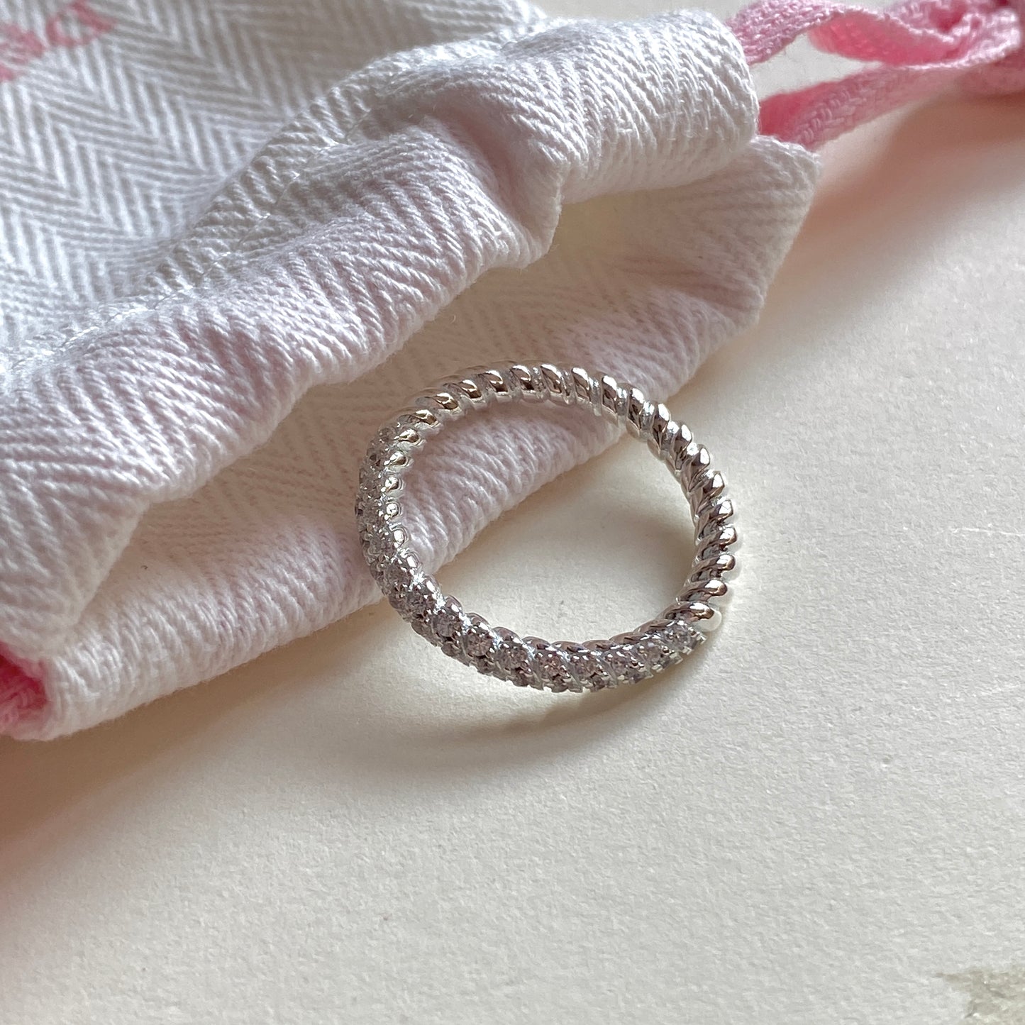 Sterling silver twisted ring centered on a white herringbone pouch with pink drawstrings.