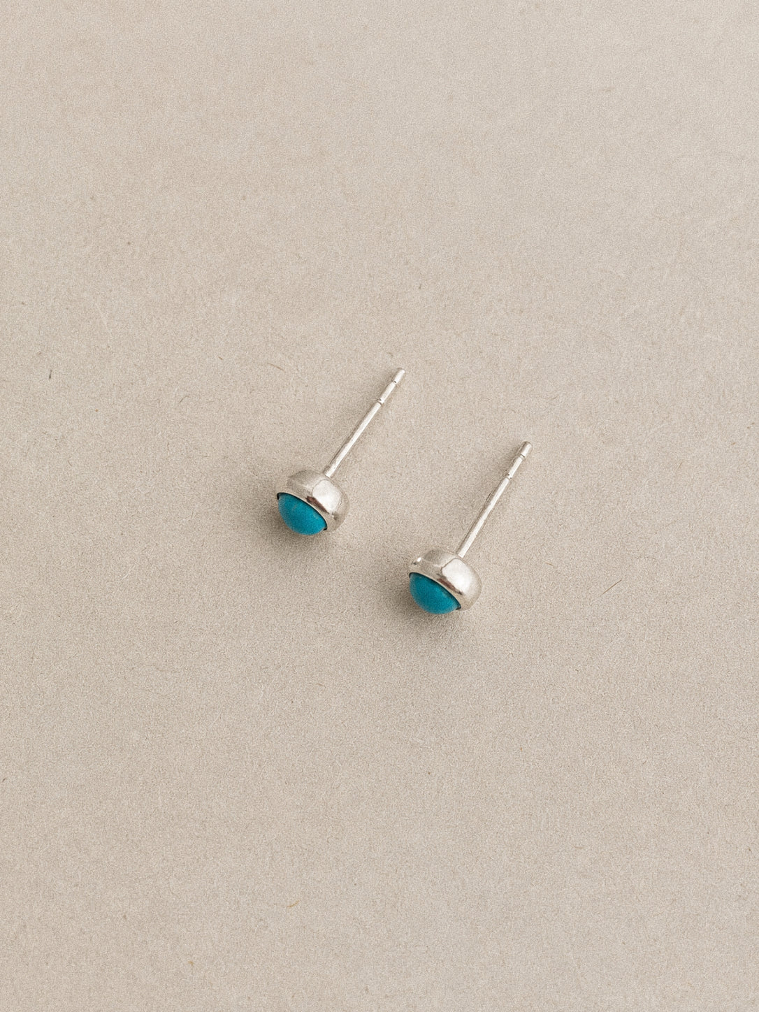 Angled close view of turquoise stud earrings showing their smooth silver bezels and slim sterling posts.