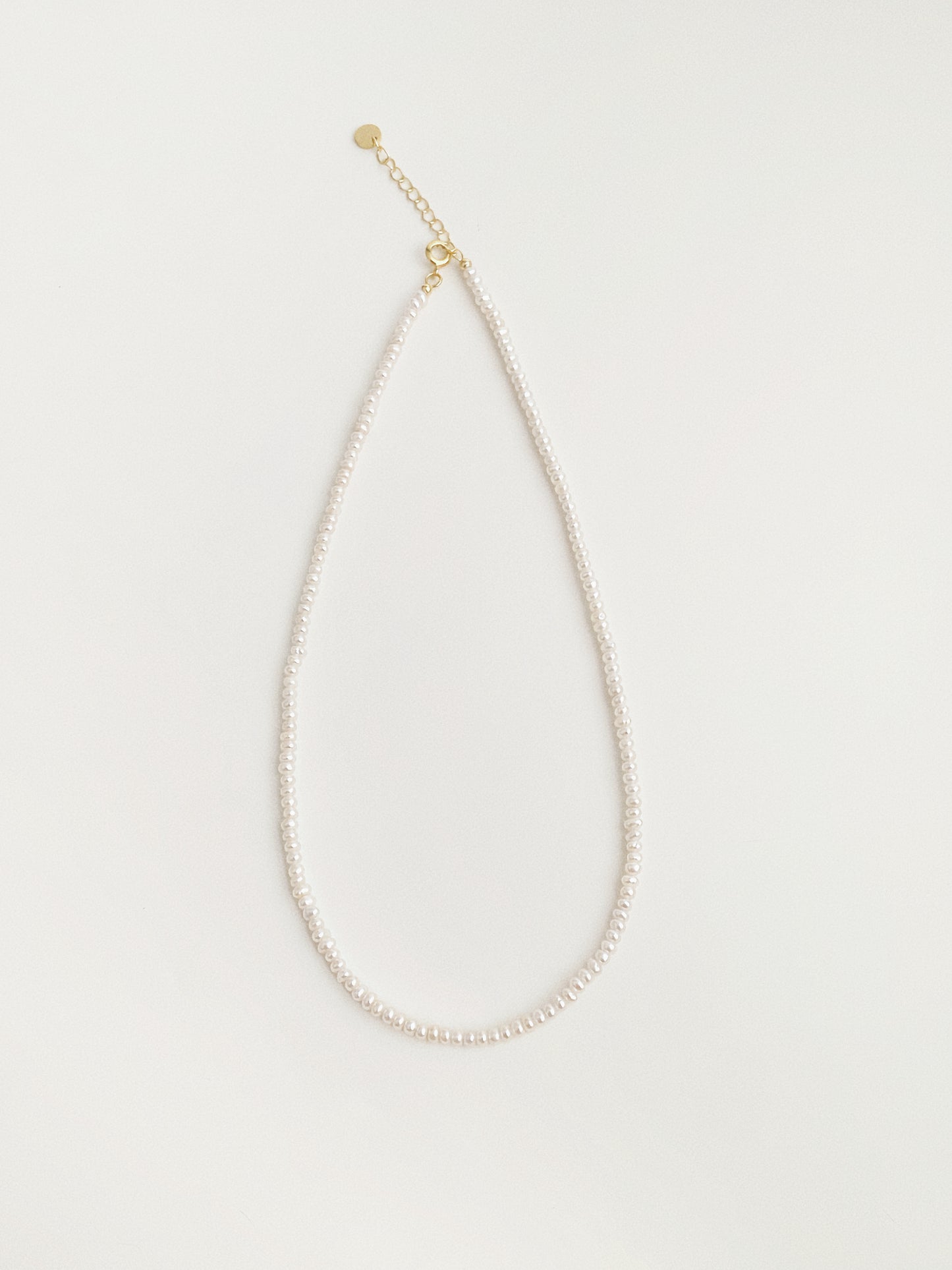 Small freshwater pearl choker necklace shown hanging with gold extension chain and tag detail