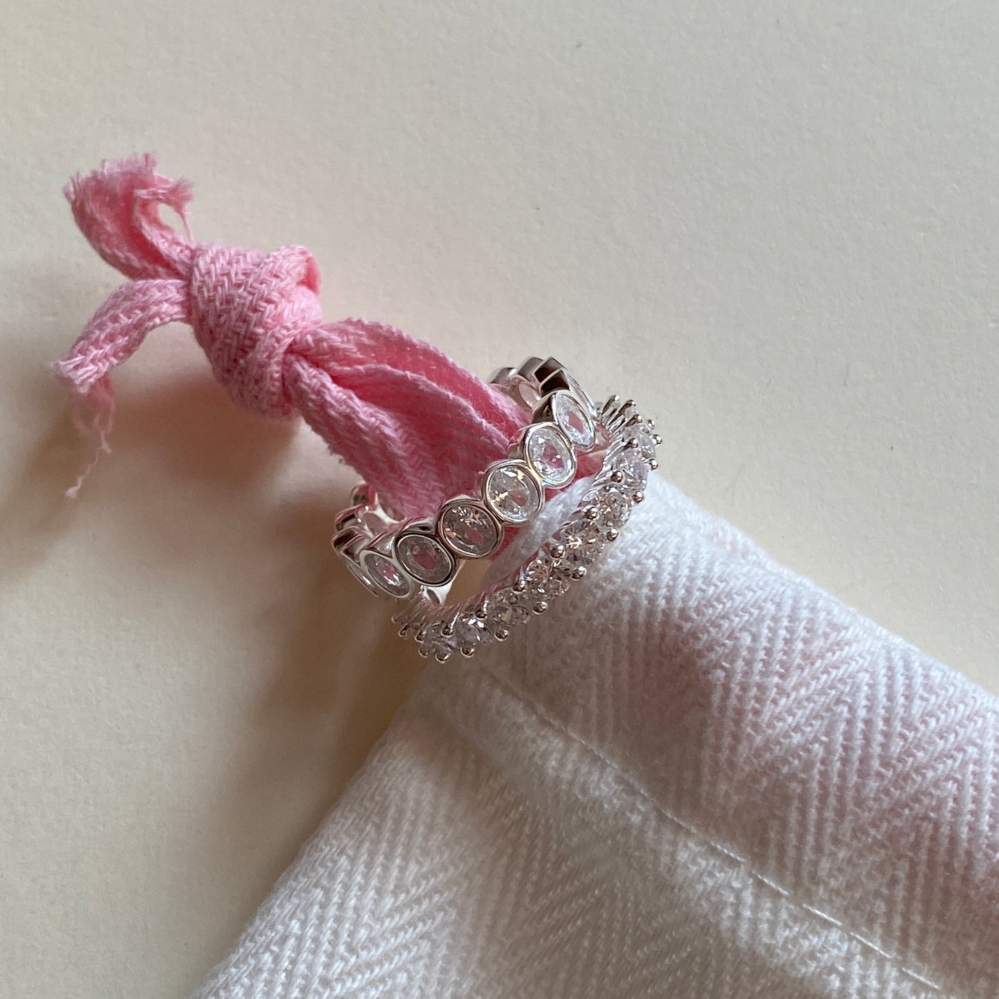 Two sterling silver stackable rings displayed on pink drawstring jewelry pouch.
