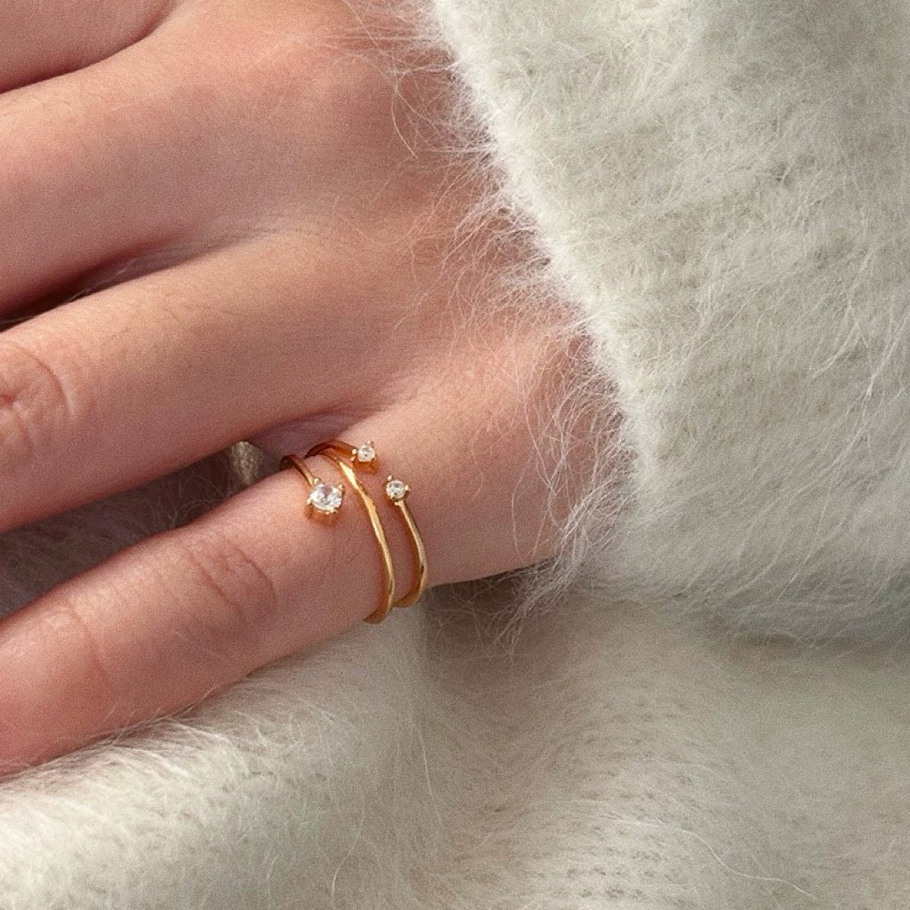 Stack of dainty gold rings with cubic zirconia on hand in soft knit jumper