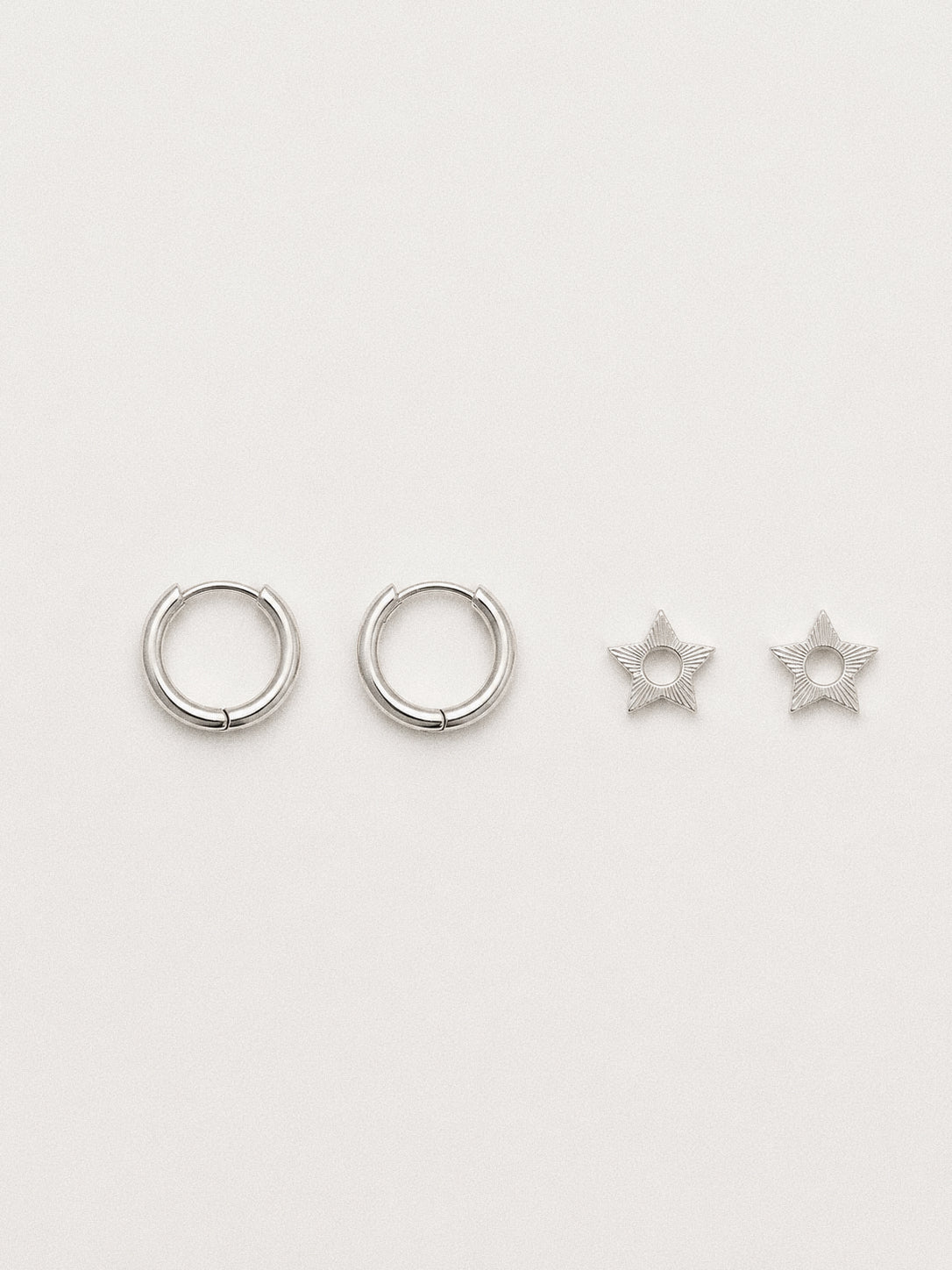 Silver Nova huggie hoops shown beside their two removable engraved star charms, wearable with or without.