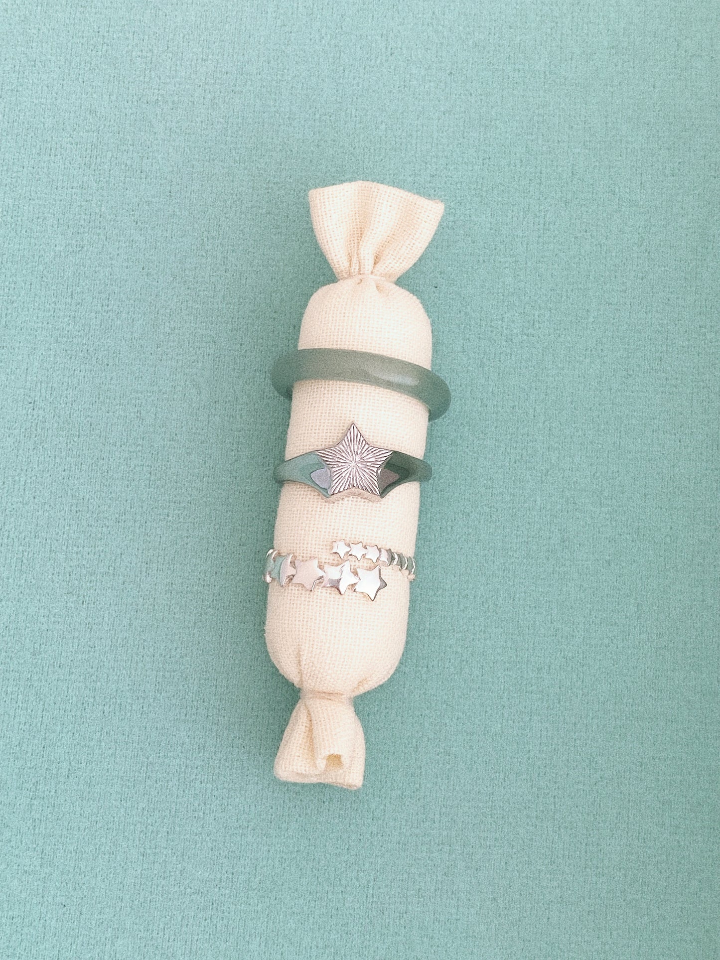 Silver star signet ring wrapped around fabric with a star bead bracelet, styled on a soft green backdrop.